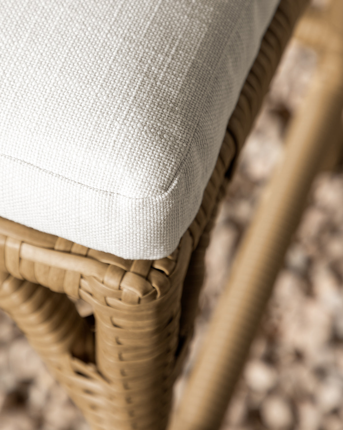 Close-up of the Makerspalm Marisol Indoor/Outdoor Counter Stool (Set of 2), featuring handwoven wicker and a light textured cushion, shown with a blurred pebble background. McGee & Co.