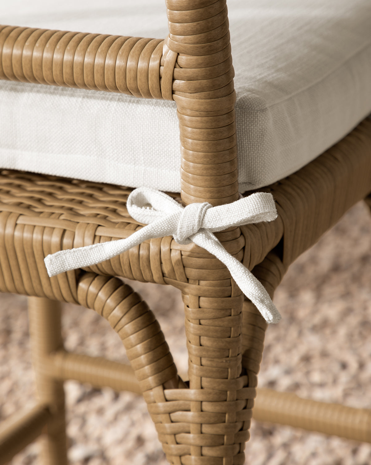 Close-up of the Makerspalm Marisol Indoor/Outdoor Counter Stool (Set of 2), featuring handwoven wicker, a white seat cushion secured with a fabric bow, and set on a textured beige carpet. McGee & Co.