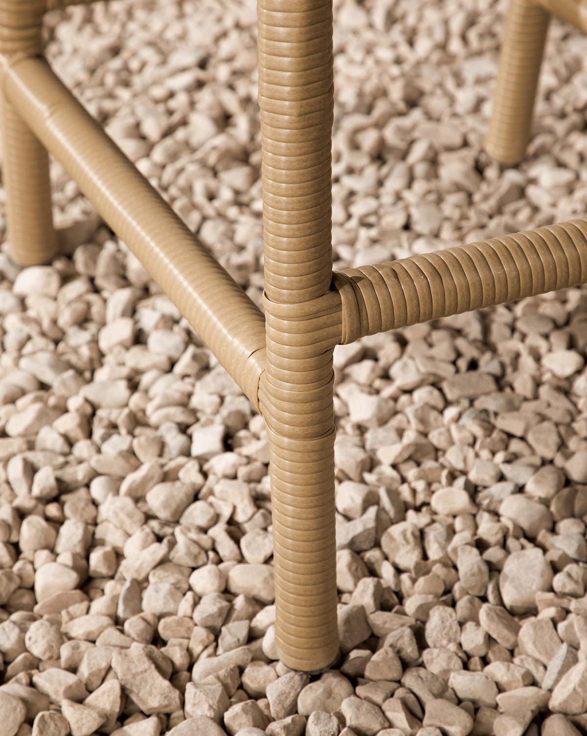 Close-up of tan, textured legs from the Makerspalm Marisol Indoor/Outdoor Counter Stool (Set of 2), standing on a bed of small, light beige pebbles. McGee & Co.