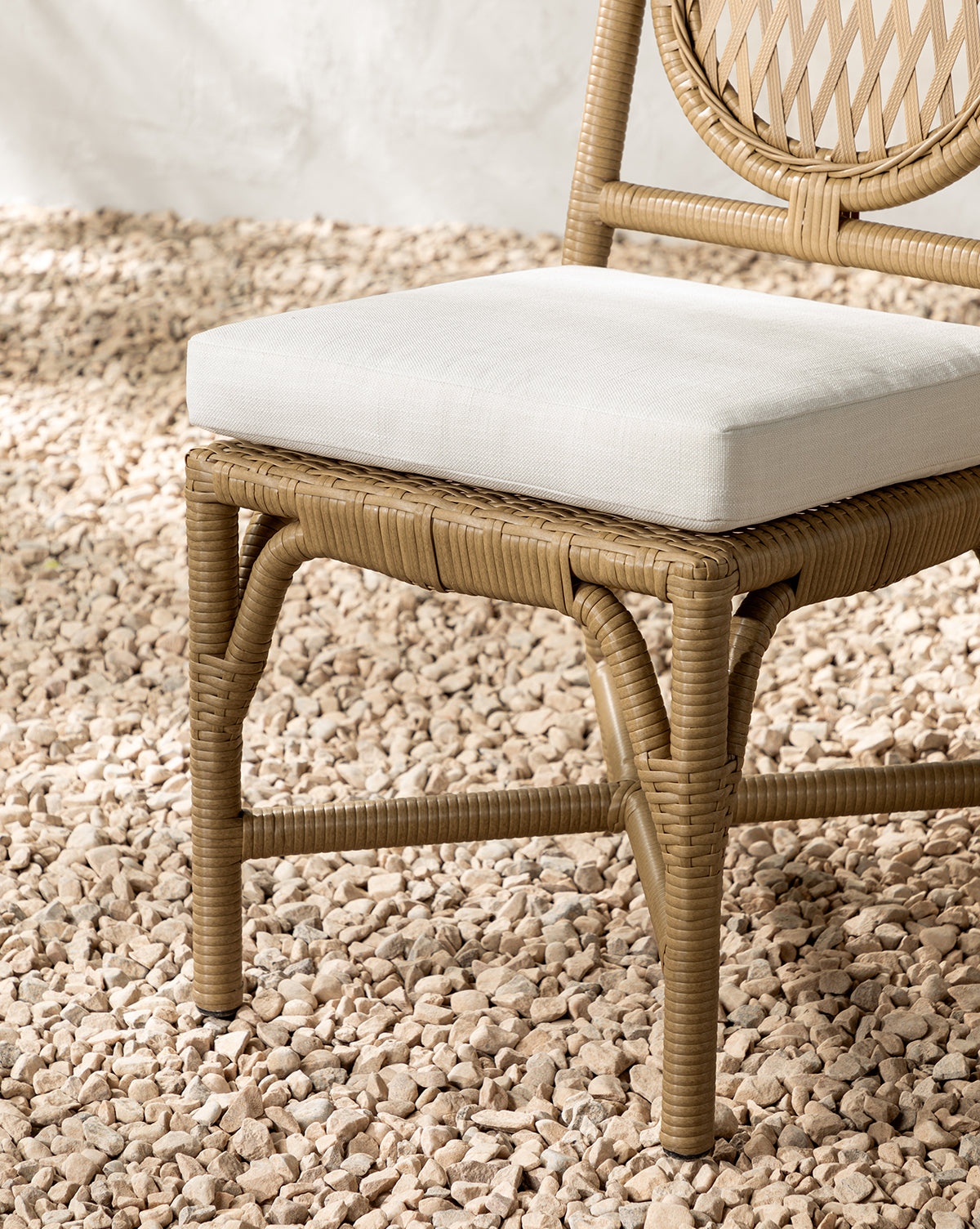 A close-up of the Marisol Indoor/Outdoor Dining Chair (Set of 2) with light beige cushions, shown on a bed of pale pebbles against a white wall—an ideal choice for your outdoor dining setup, by McGee & Co.