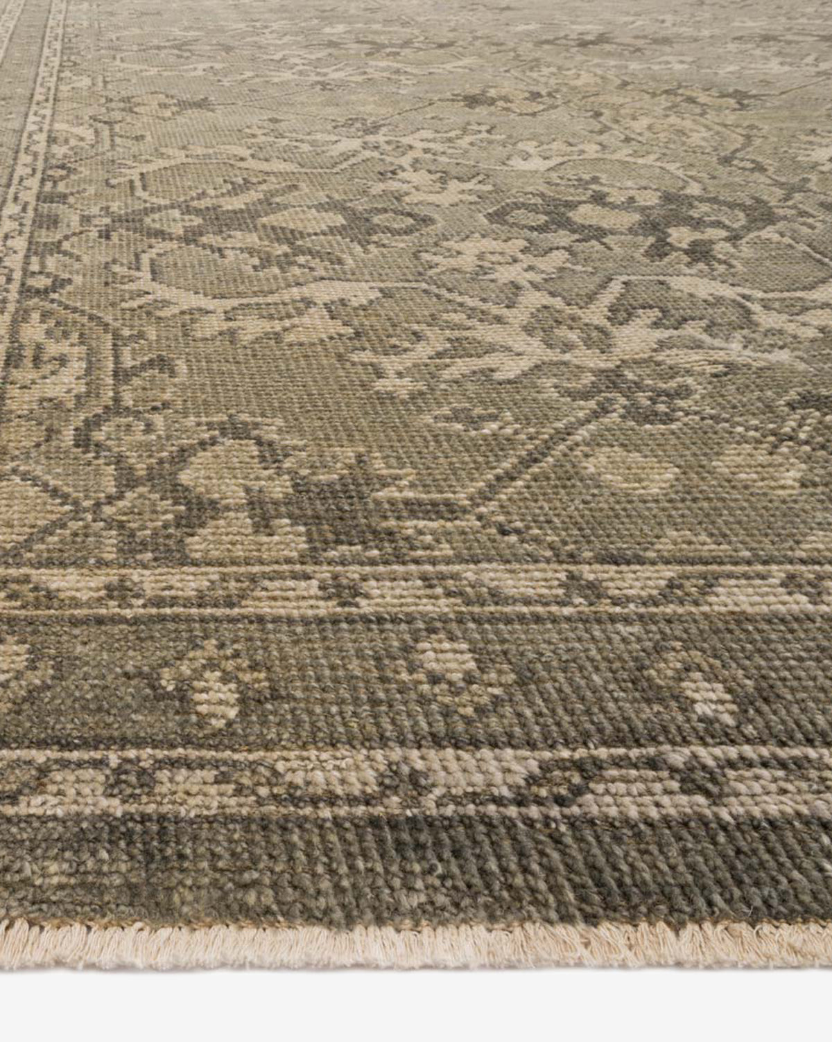 A close-up of the Marola Hand-Knotted Wool Rug shows its durable, intricate faded floral and geometric patterns in muted green, beige, and brown hues, with a visible border and fringed edge, by McGee & Co.