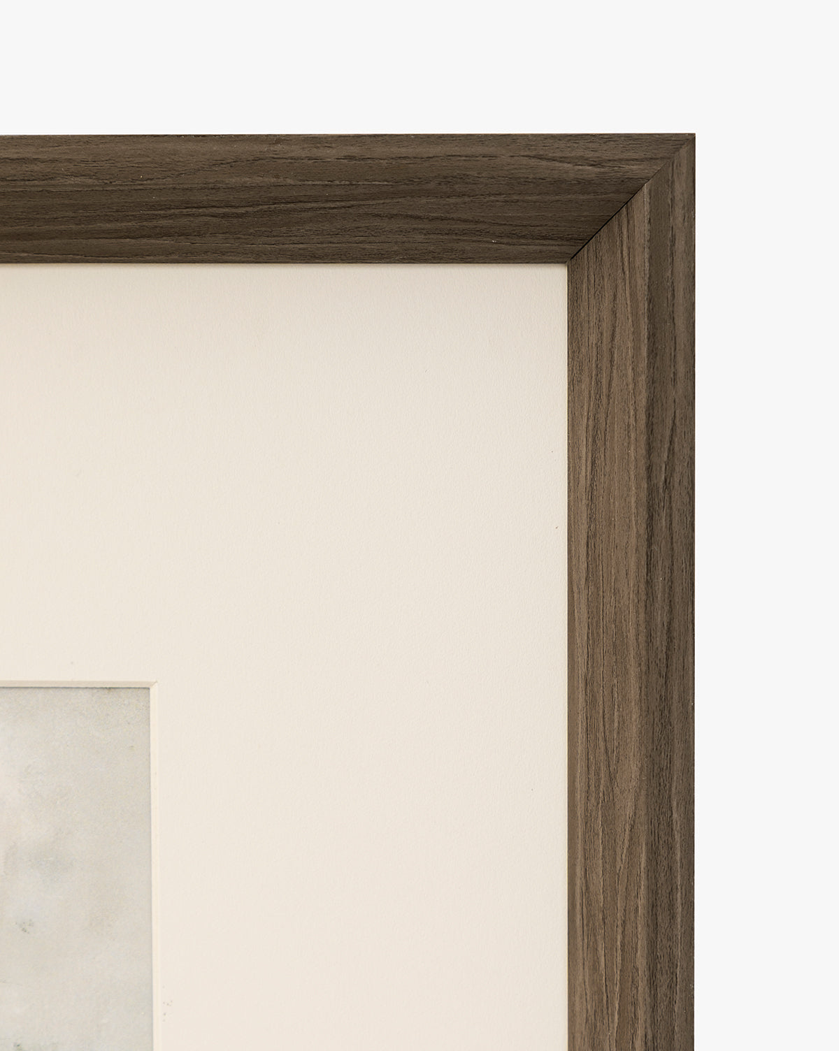 Close-up of the top right corner of a walnut woodgrain frame with a white mat and partially visible Marshland artwork, set against a plain white background, by McGee & Co.