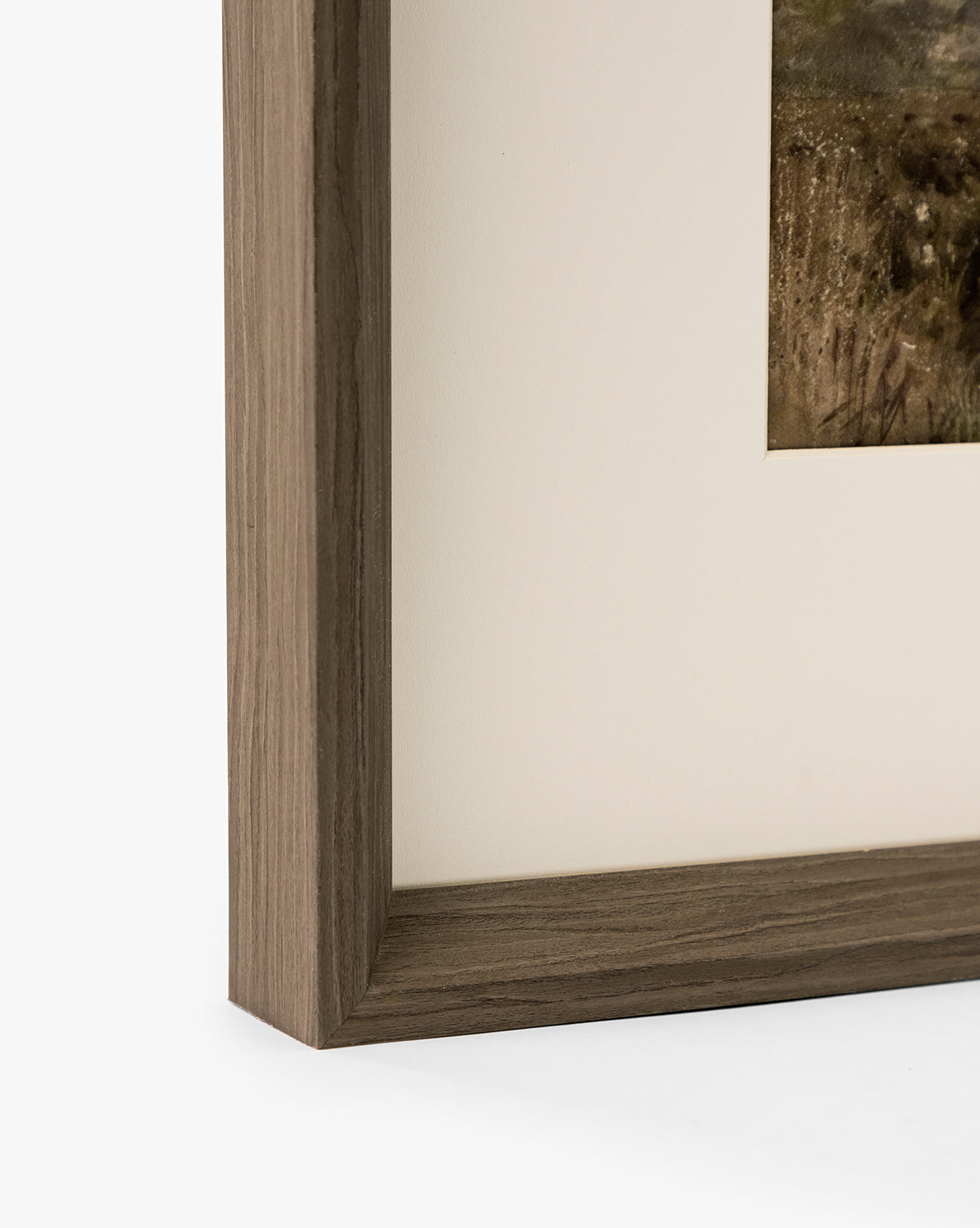 Close-up of the corner of a walnut woodgrain frame with a light brown finish, showcasing part of the Marshland matted giclee on paper against a white background, by McGee & Co.