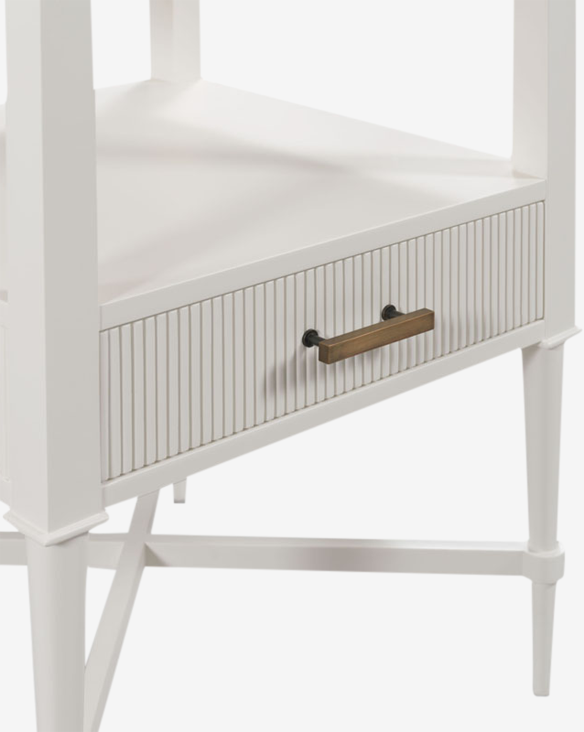 A close-up of the Martinez Nightstand shows a modern white side table with slender legs, an open shelf, a reeded drawer front, and brass hardware that highlight its minimalistic design by McGee & Co.