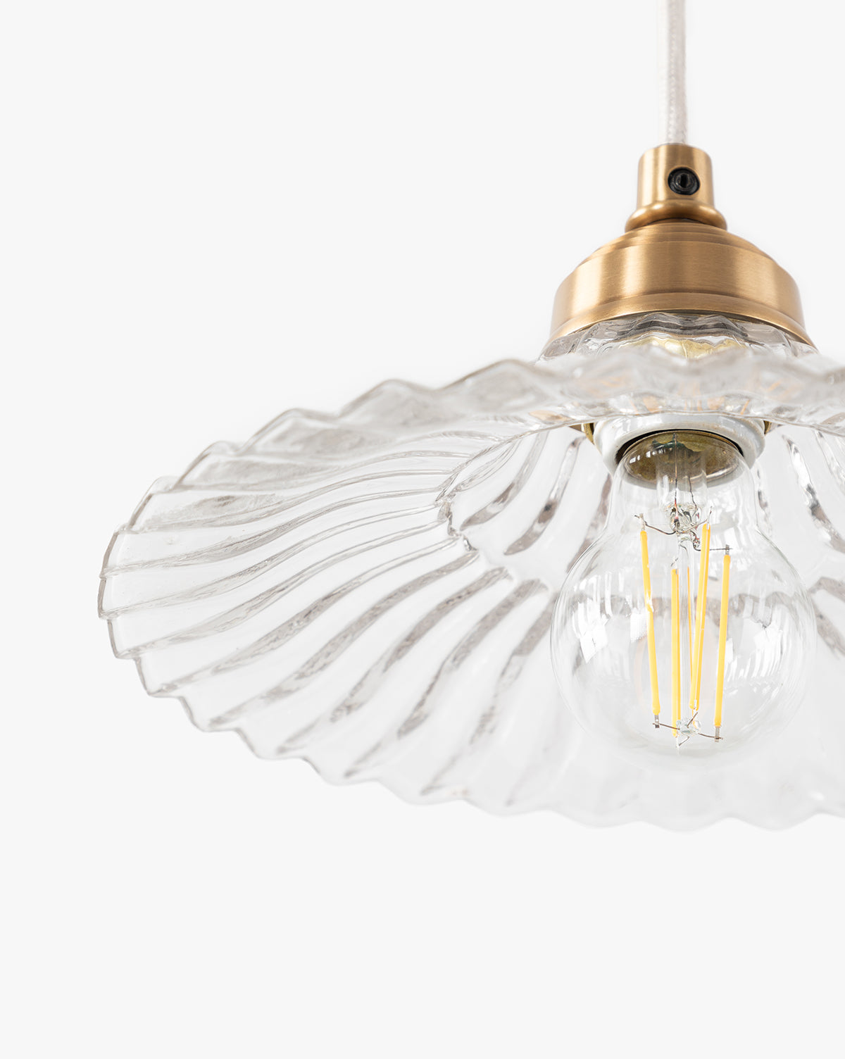 A close-up of the McGee & Co. x Loeffler Randall Maude Glass Pendant, showcasing its clear wavy glass shade, vintage-style exposed filament bulb, and elegant brass hardware set against a plain white background, by McGee & Co.