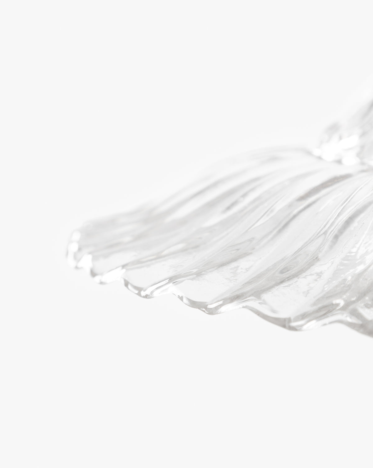 Close-up of a transparent, wavy glass shade with smooth lines on a white background. Its sculpted edge recalls the McGee & Co. x Loeffler Randall Maude Glass Pendant, ideal for bringing elegance to any space by McGee & Co.