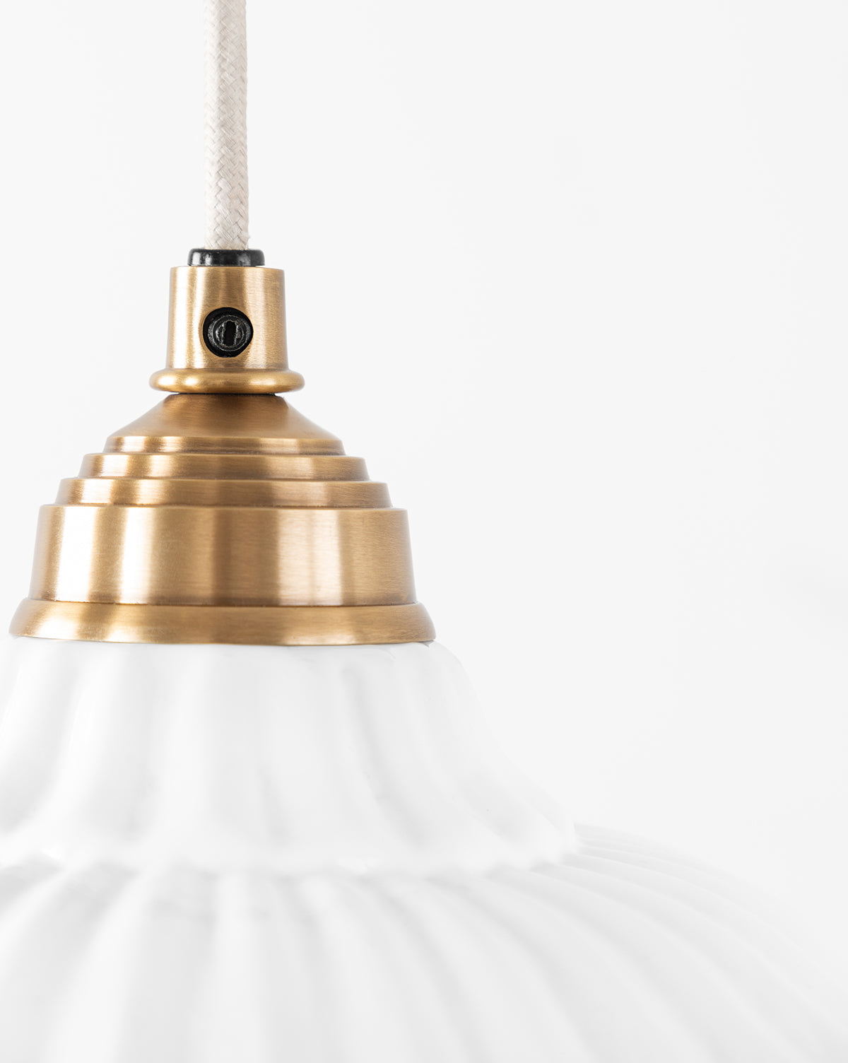 Close-up of the McGee & Co. x Loeffler Randall Maude Glass Pendant, showcasing its ribbed white glass shade and brass hardware, hanging by a white cord against a plain white background, by McGee & Co.