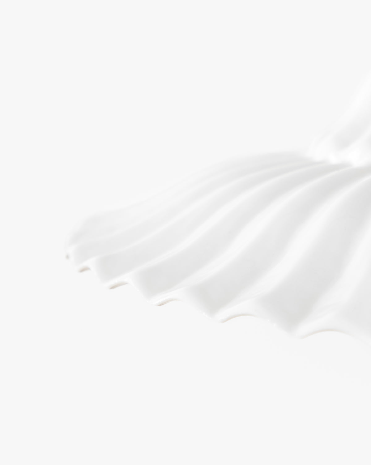 Close-up of a white, scalloped, shell-shaped ceramic plate set against a plain background, echoing the elegant curves of the McGee & Co. x Loeffler Randall Maude Glass Pendant with brass hardware, by McGee & Co.