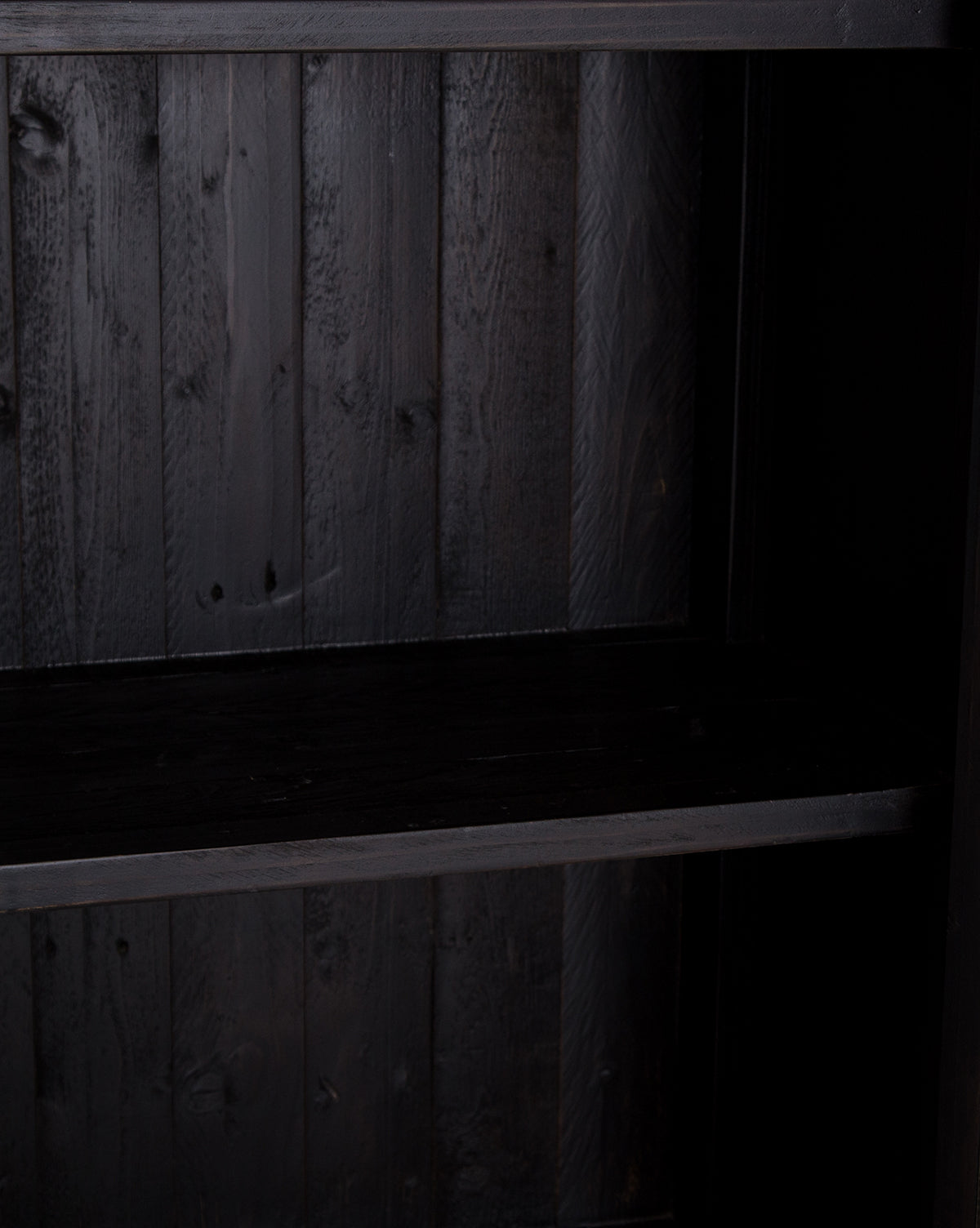 A close-up of the Maverick Cabinet, an empty dark wooden shelf with a vertical panel background that highlights its natural grain. Sturdy reclaimed pine construction and iron hardware give this piece a timeless look by McGee & Co.