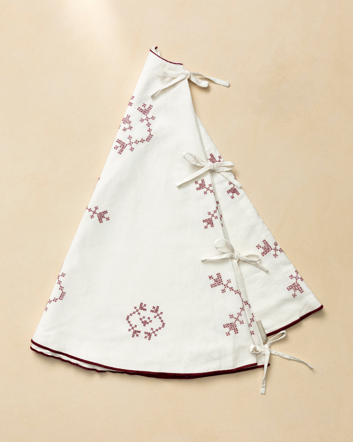The McCallister Tree Skirt is a white, triangular vintage piece with red embroidered snowflakes, maroon trim, and four white ribbon ties—perfect for bringing heirloom charm to your holiday decor, by McGee & Co.