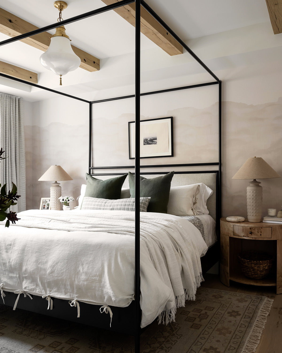 A modern bedroom with a black canopy bed, the Easton Striped Duvet Cover in cream and oatmeal, green accent pillows, wooden ceiling beams, two beige lamps on wooden nightstands, and framed artwork above the bed.