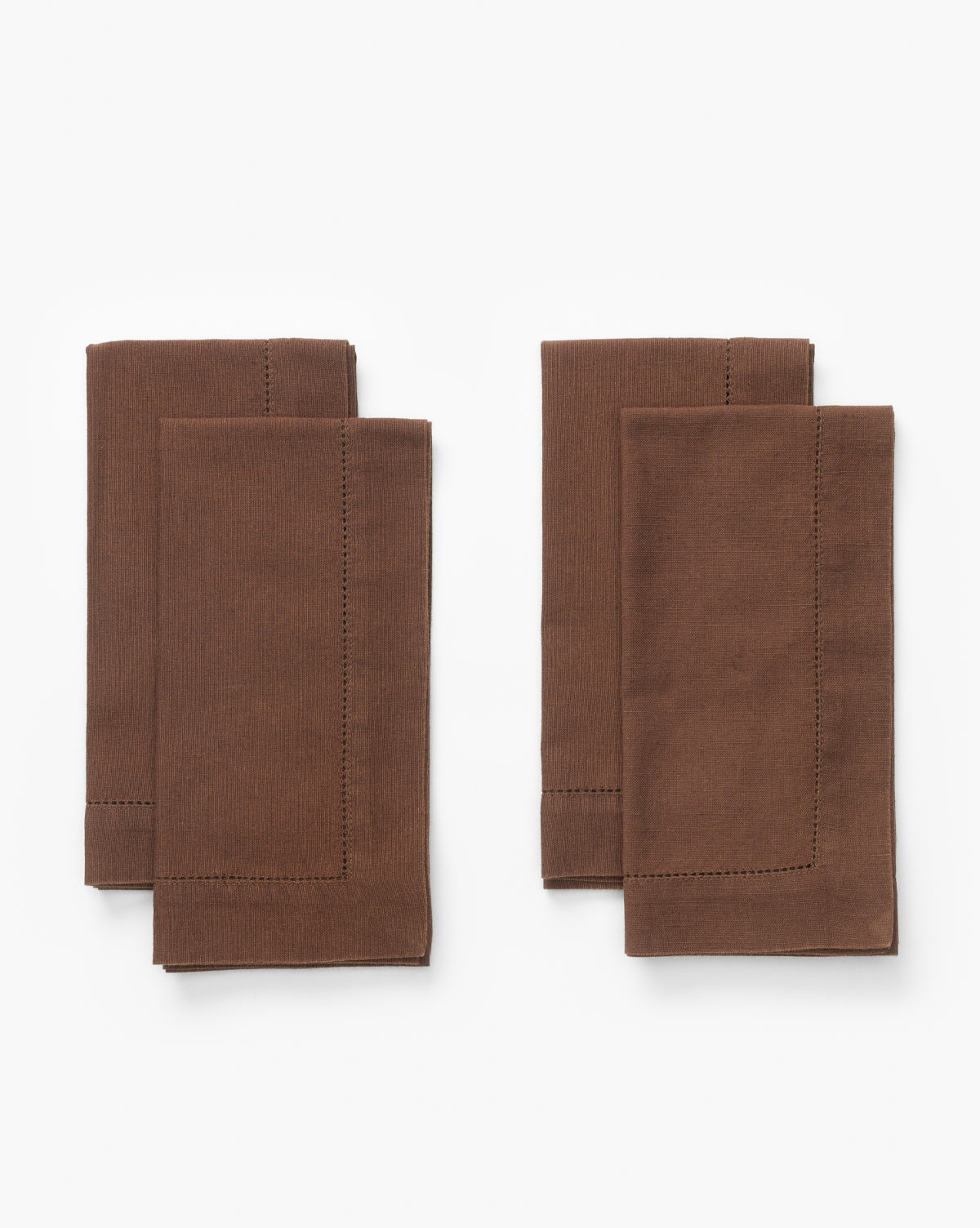 A set of four brown Melita Napkins, each with decorative stitching, is arranged in two pairs on a plain white background, by McGee & Co.