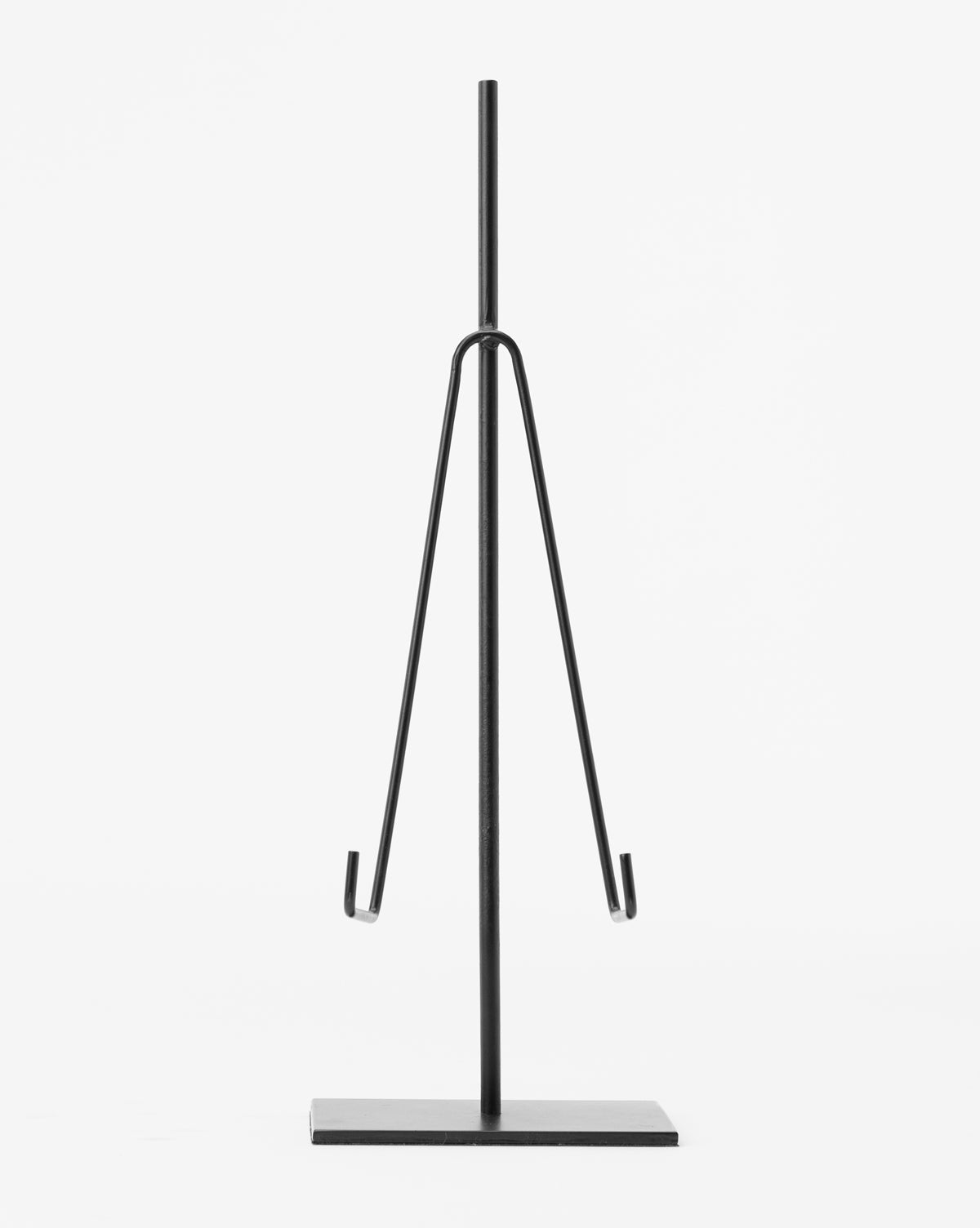 The Metal Easel features a minimalist black metal design with a vertical rod, two angled arms with small hooks, and a flat rectangular base—perfect for art display or decor. Shown against a plain white background.