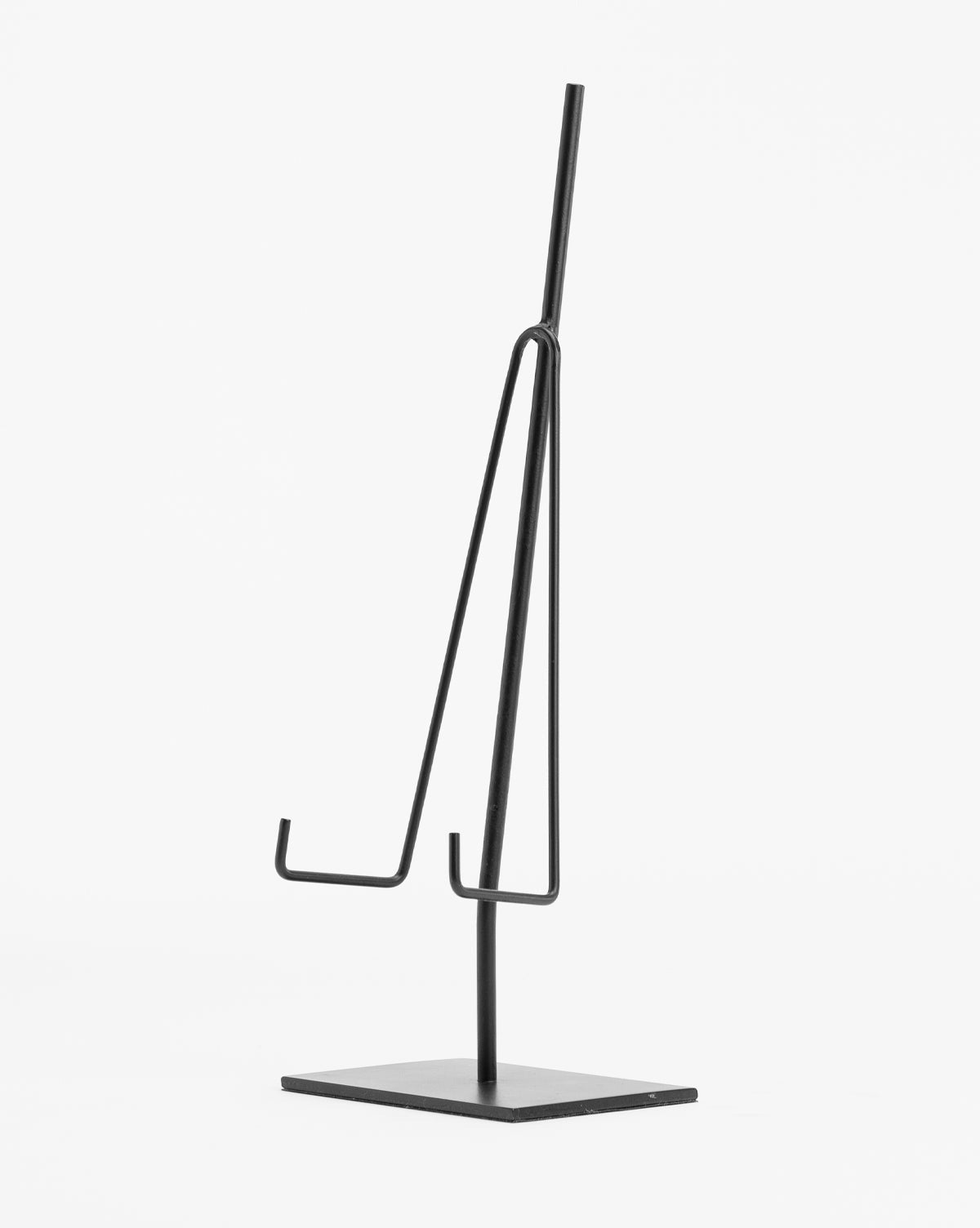 The Metal Easel features a minimalist black metal design with a square base and two angled hooks, ideal for displaying items as a decorative easel. Shown on a plain white background.