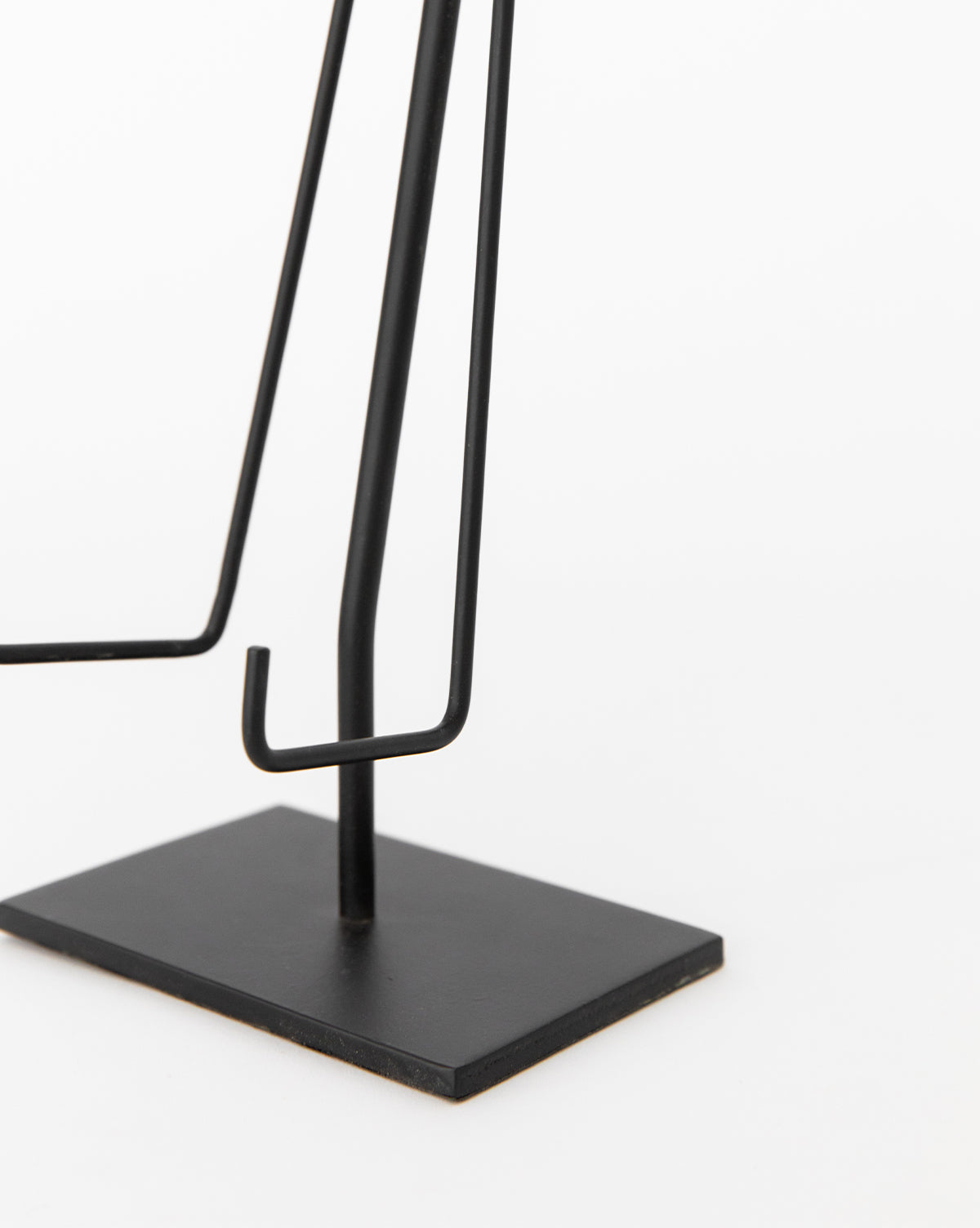 A close-up of the Metal Easel, featuring a minimalist black metal design with a rectangular base and angular supports, set against a plain white background.
