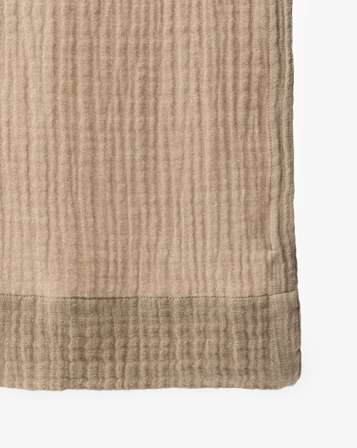 A close-up of the Mirella Shower Curtain shows its light brown, textured fabric with a subtle grid pattern and a darker hem at the bottom edge, set against a white background.