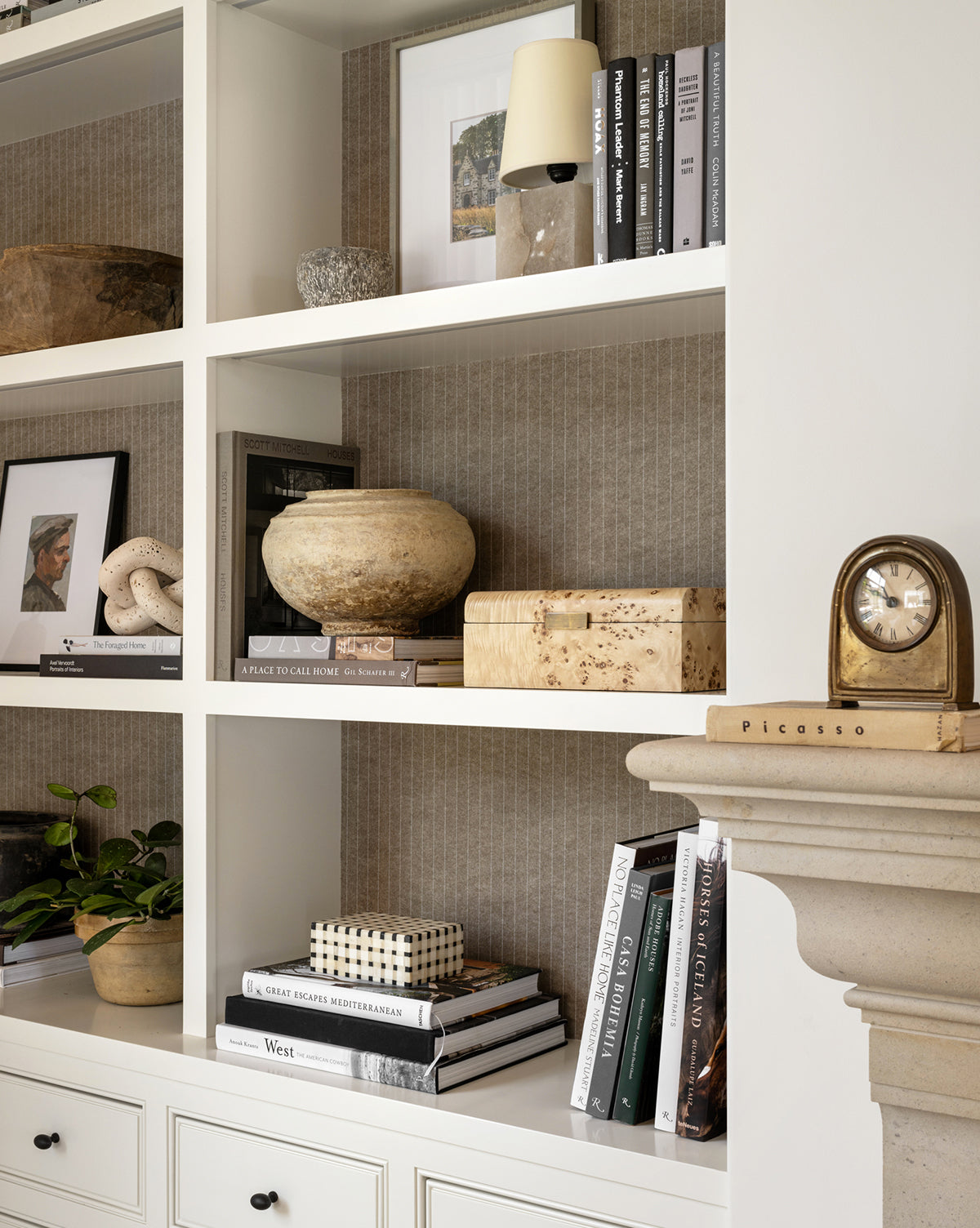 A styled bookshelf with books, a Grid Patterned Box, pottery, framed photos, a small plant, clock, and ornaments on white shelves—perfect for adding classic home decor flair.