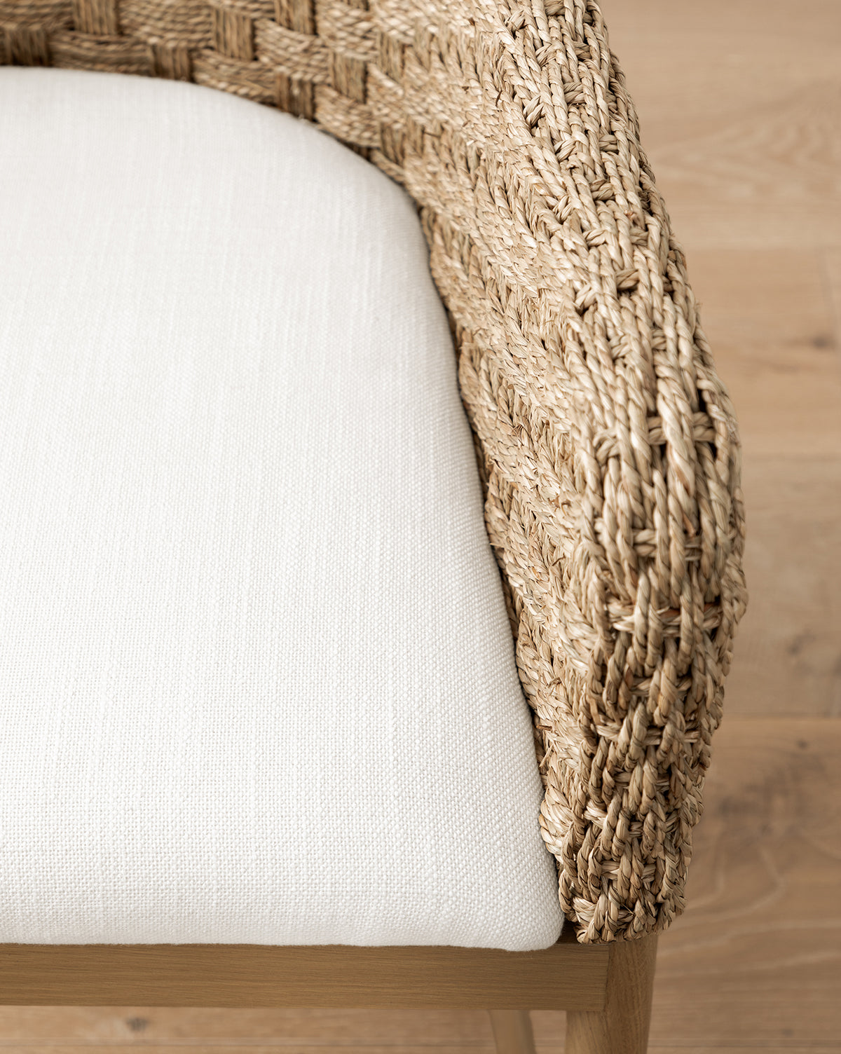 Close-up of the Molly Arm Chair, a modern seat with textured woven rattan armrests and a light beige fabric cushion, shown on a light wooden floor, by McGee & Co.