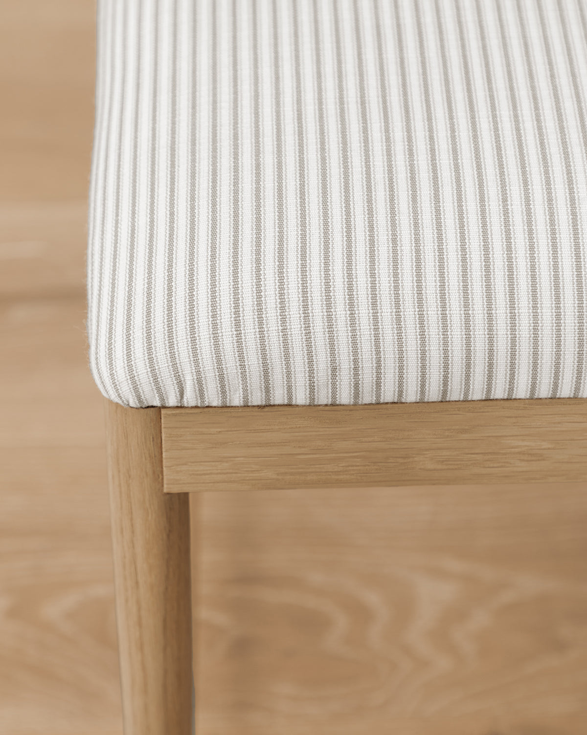 Close-up of the Molly Stools corner, featuring a cushioned seat in white and light gray vertical stripes, supported by sturdy solid oak legs on a wooden floor, by McGee & Co.