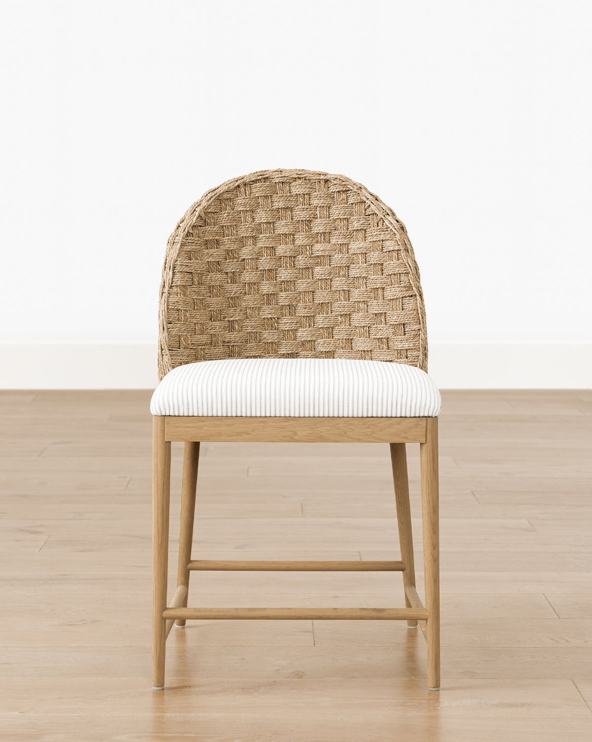The Makerspalm Molly Dining Chair showcases a solid oak frame, woven rattan backrest, and striped cushioned seat, elegantly placed on a light wood floor against a plain white wall. McGee & Co.