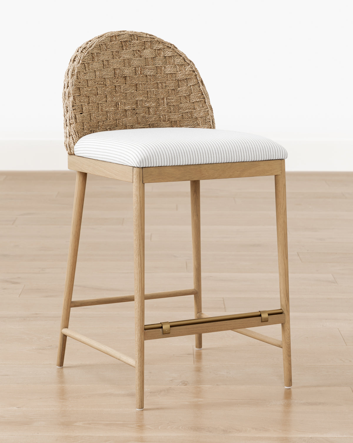 The Molly Stool, crafted from solid oak, features a natural finish, a woven rattan curved backrest, and a white cushioned seat, by McGee & Co. It is shown on a light wood floor against a plain white wall.