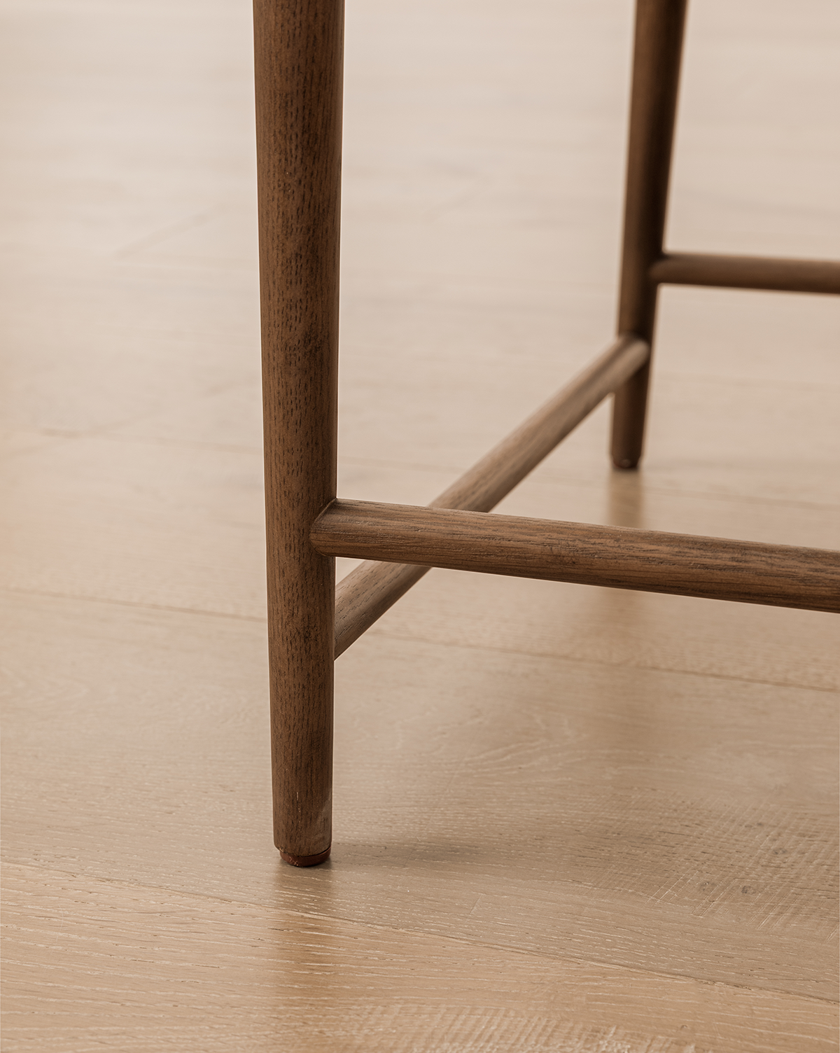 Close-up of the Molly Dining Chair leg with a horizontal support bar on a light wood floor, highlighting its simple, clean lines and natural solid oak texture, by McGee & Co.