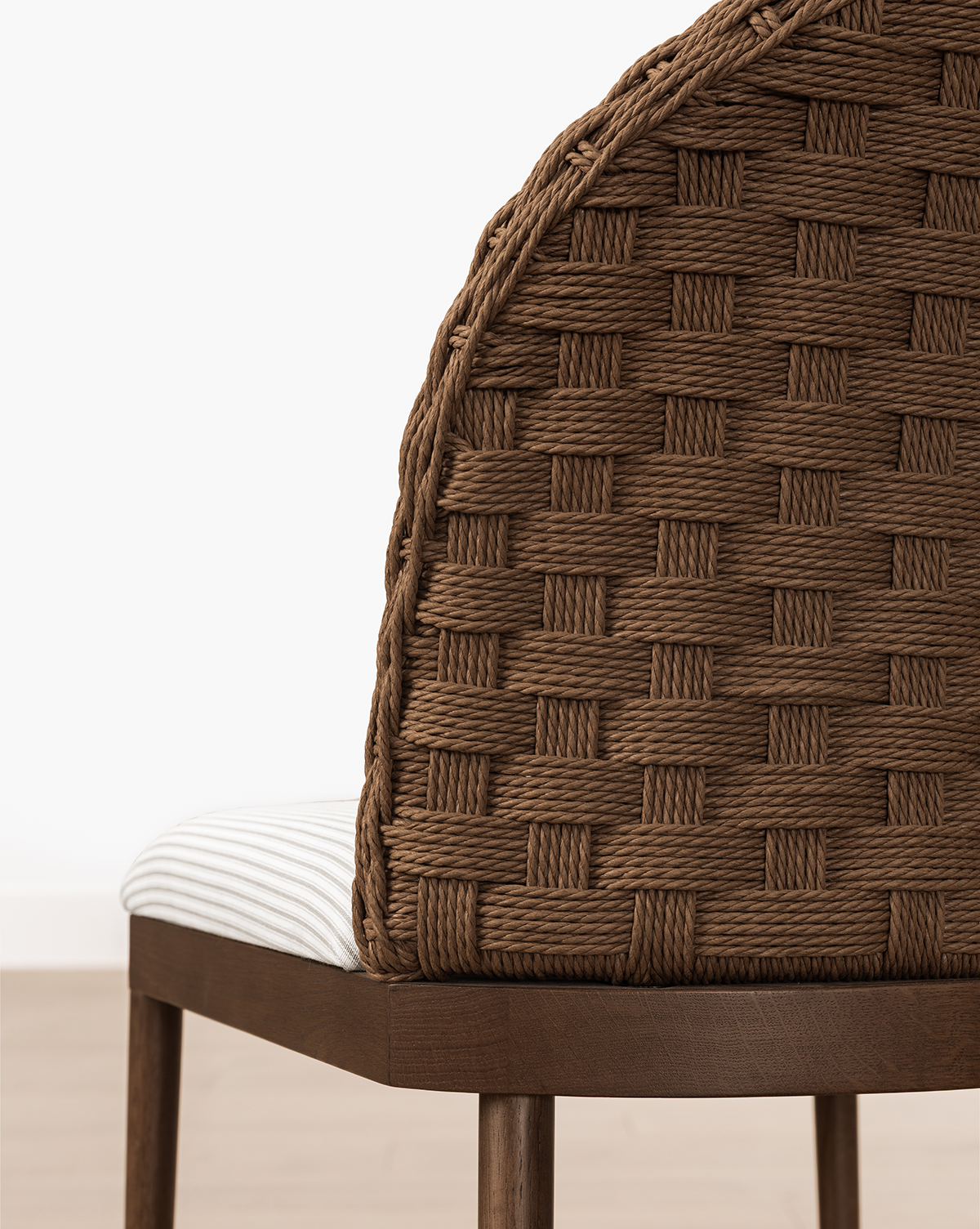 A close-up of the Molly Stool, showcasing its curved, woven brown backrest and white striped cushioned seat on solid oak legs, set against a light floor and white wall, by McGee & Co.