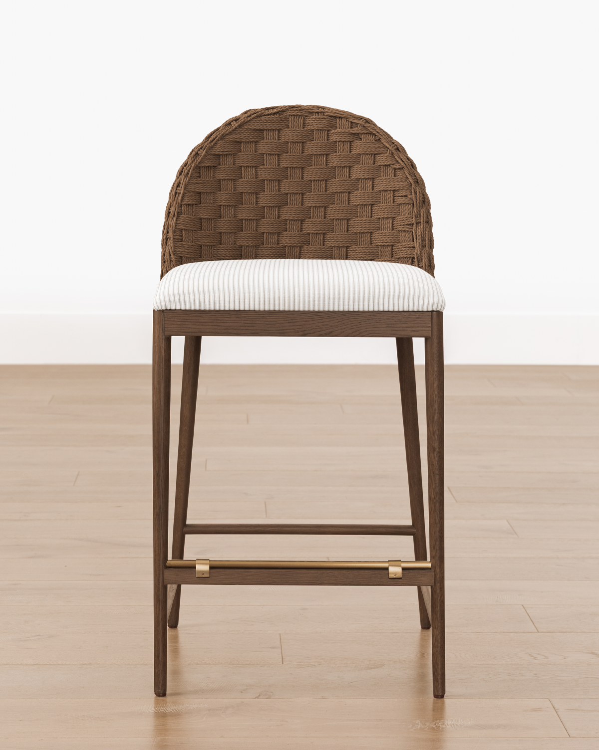 The Molly Stool features a woven brown curved backrest, striped cushioned seat, and solid oak legs with gold accents, standing on a light wood floor against a white background, by McGee & Co.