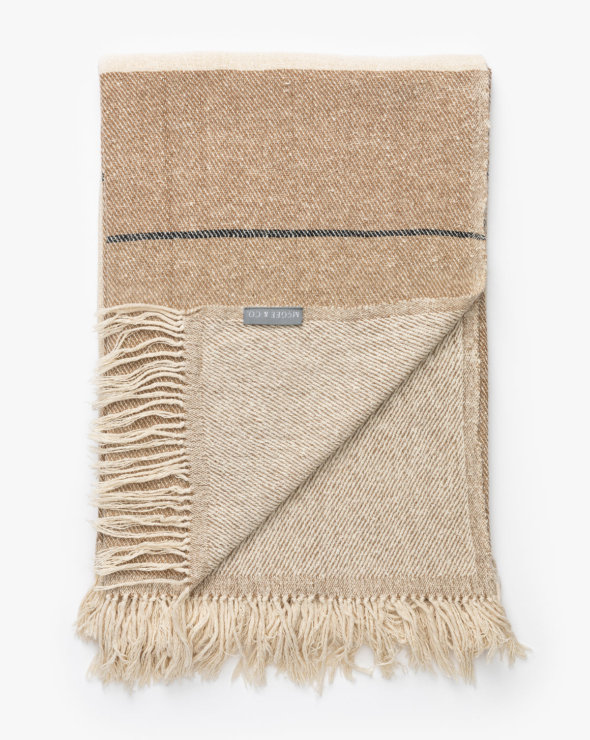 The Murphy Silk Throw is a hand-loomed, beige and tan two-tone blanket with fringed edges, featuring a horizontal stripe, visible texture, and a MOON & CO. label.