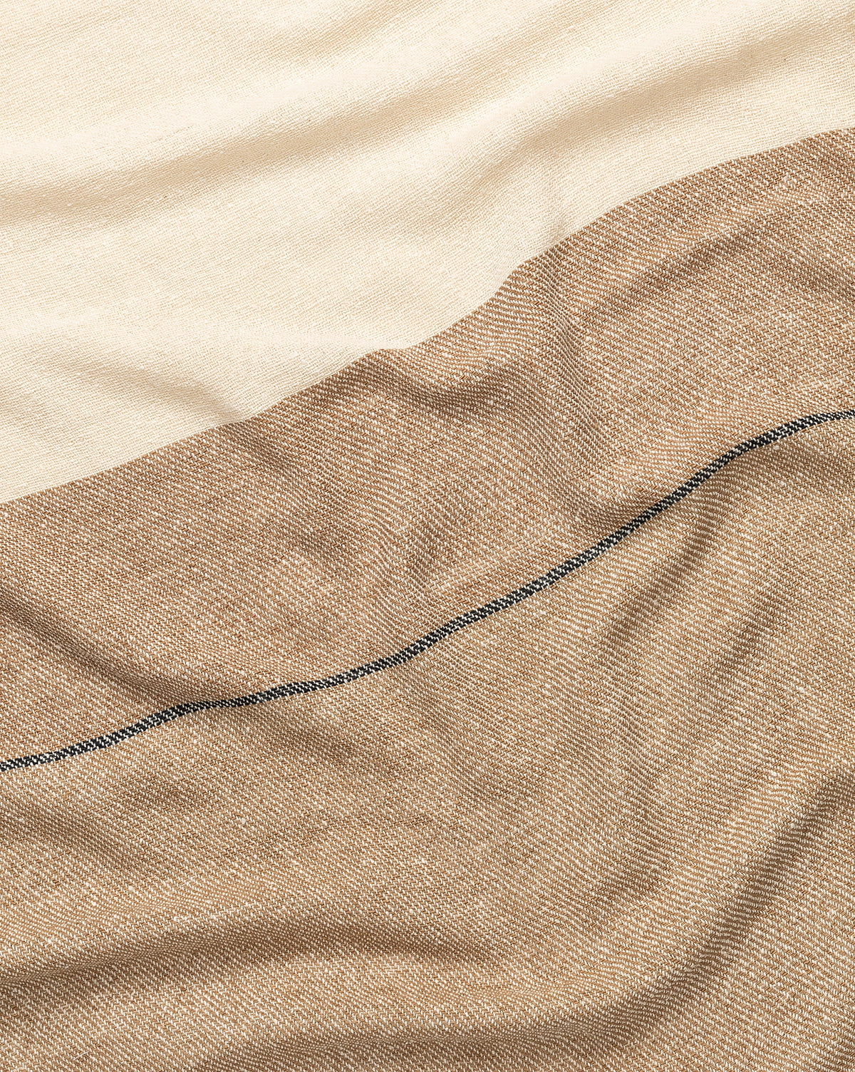 A close-up of the Murphy Silk Throw highlights its cream and light brown sections, divided by a slim dark line. Hand-loomed, the throw features gentle folds and an exceptionally soft texture.
