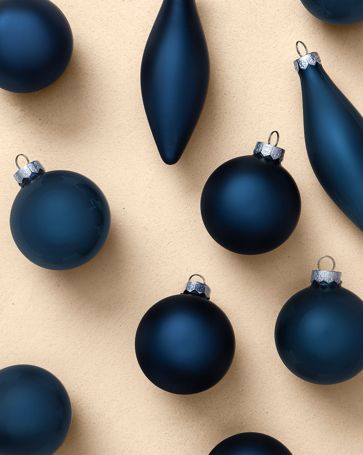Assorted Ornaments Navy (Set of 10), featuring matte round and elongated navy decorations with silver caps, are displayed across a light beige background, by McGee & Co.