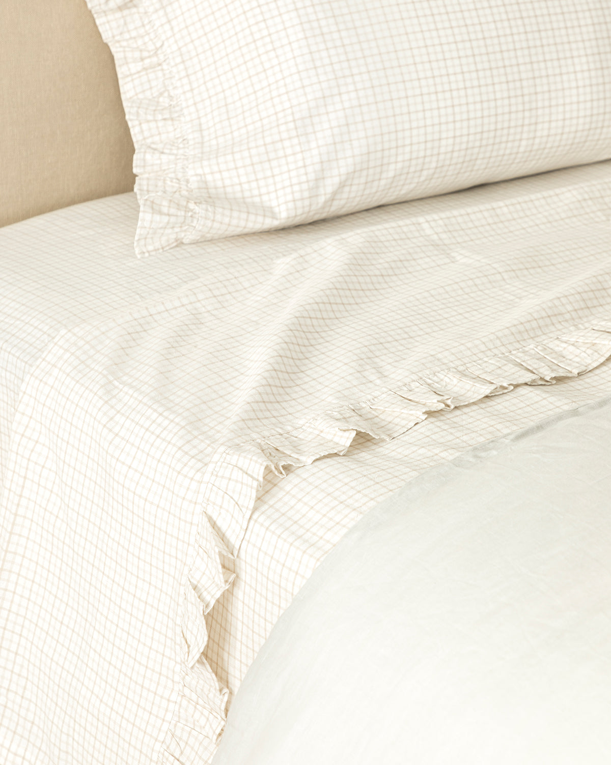 Close-up of the Nell Ruffled Twin Kids Sheet Set featuring beige and white checkered cotton bedding with subtle ruffled edges on the pillowcases, paired with a white comforter for a soft, cozy, and inviting look.