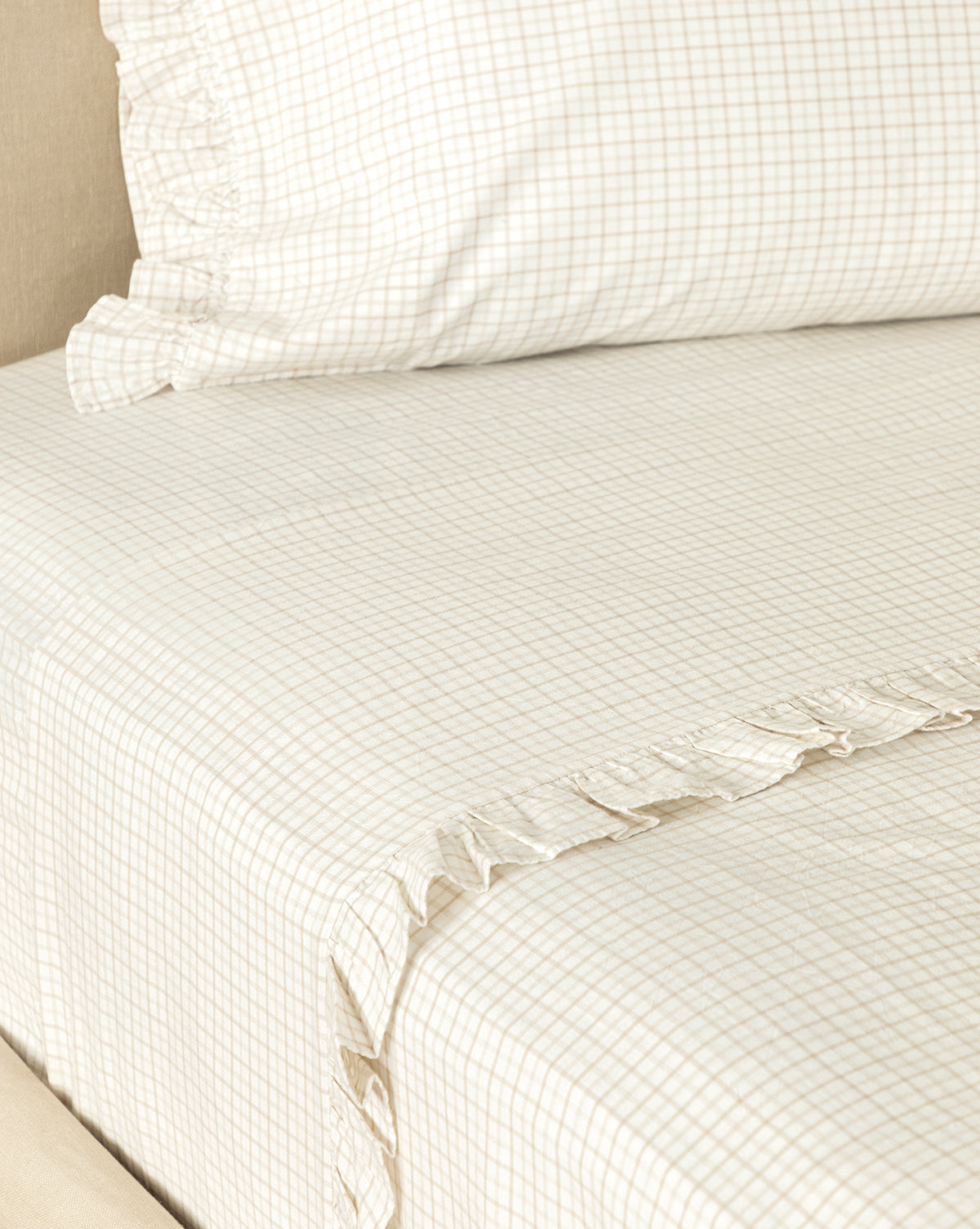 Close-up of a neatly made bed with the Nell Ruffled Twin Kids Sheet Set, featuring cream-colored cotton pillowcases and twin sheets with a small light brown checkered pattern and subtle ruffle trim along the edges.