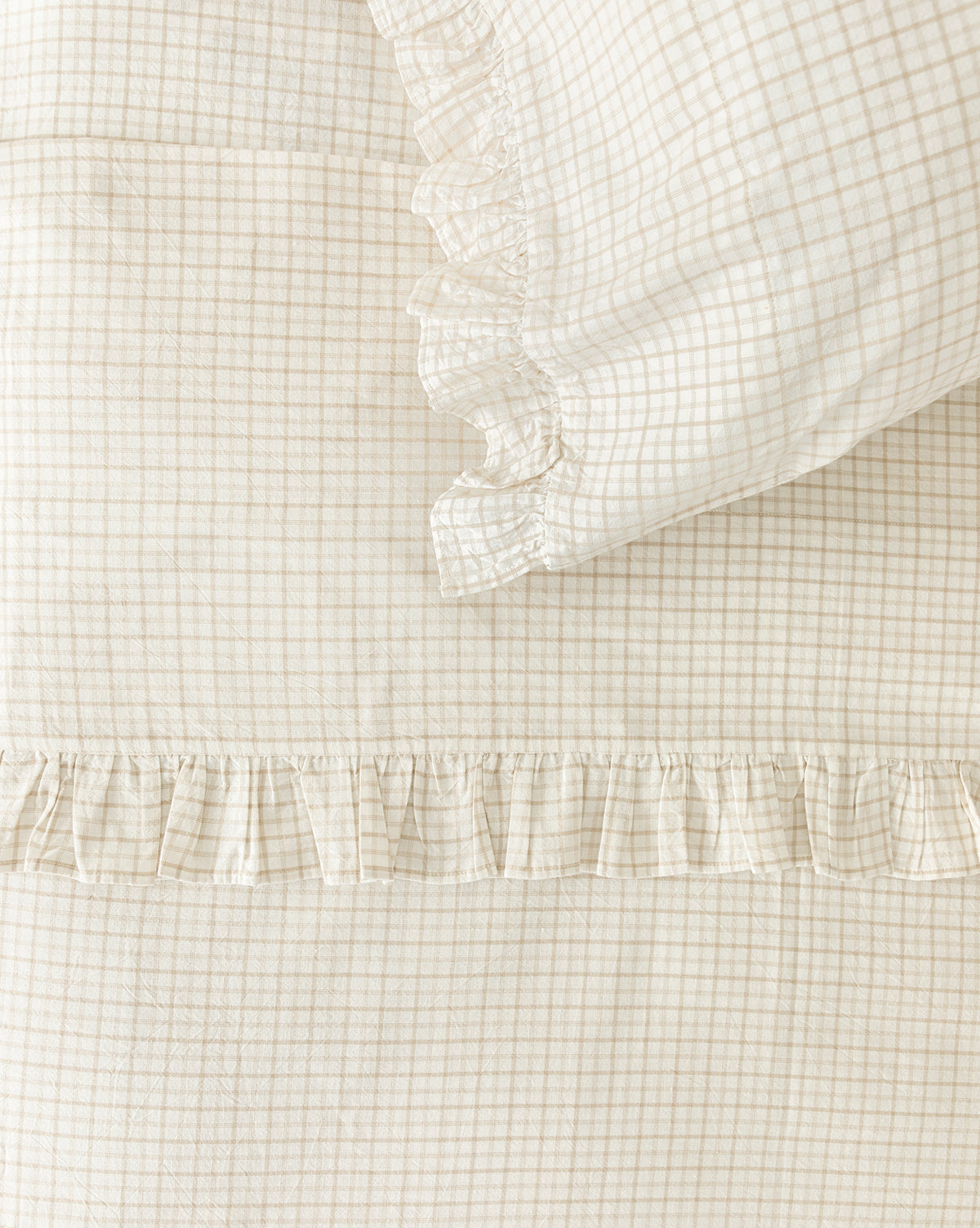 Close-up of the Nell Ruffled Twin Kids Sheet Set, featuring cream-colored cotton with a small checkered pattern and decorative ruffled trim. The fabric is soft and textured, ideal for creating a cozy space for kids.