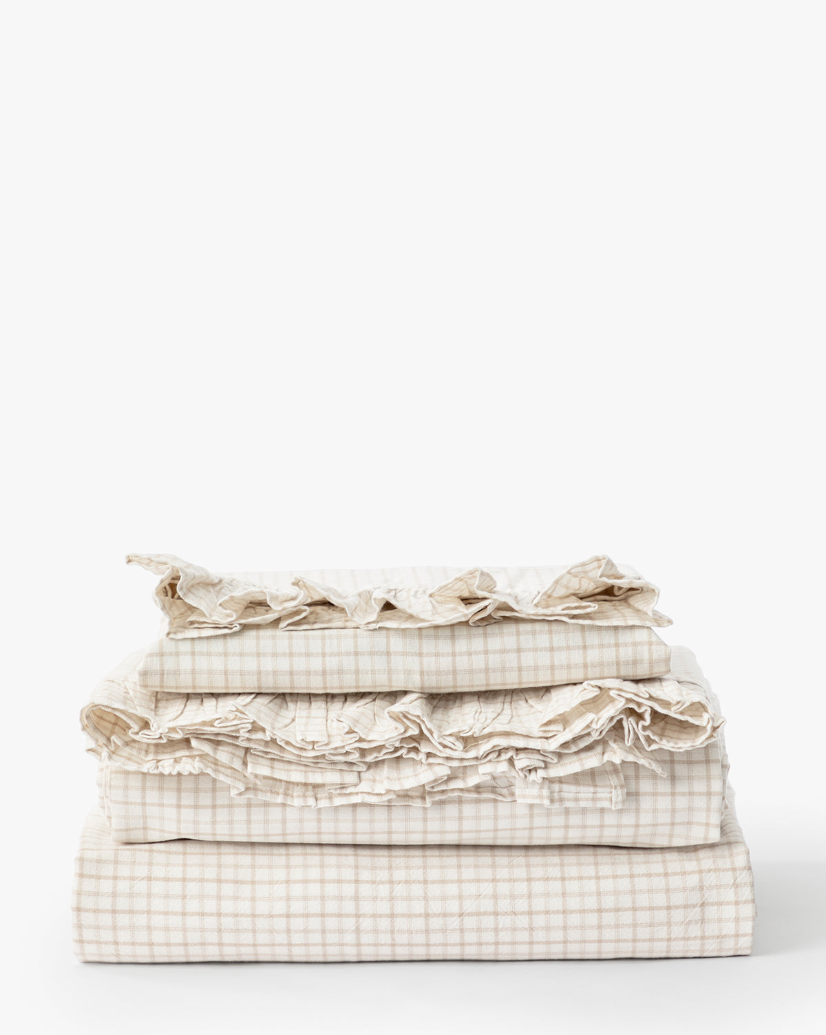 The Nell Ruffled Twin Kids Sheet Set features neatly folded beige and white gingham cotton bedding with ruffled edges, displayed against a plain white background.