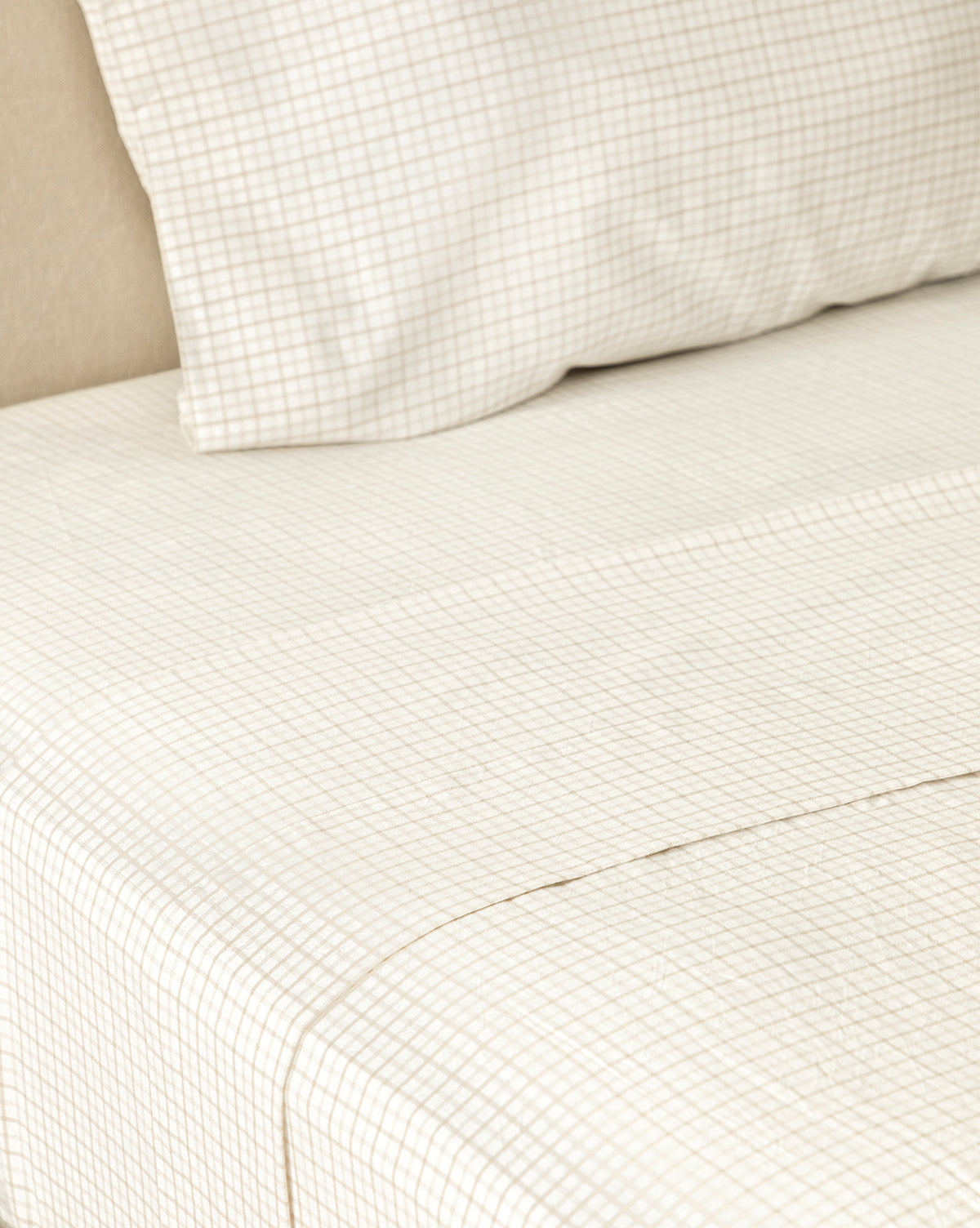 Close-up of the Nell Twin Kids Sheet Set—cream-colored cotton sheets and pillowcase with a subtle grid pattern, neatly arranged against a light upholstered headboard for a cozy children’s bedding option.