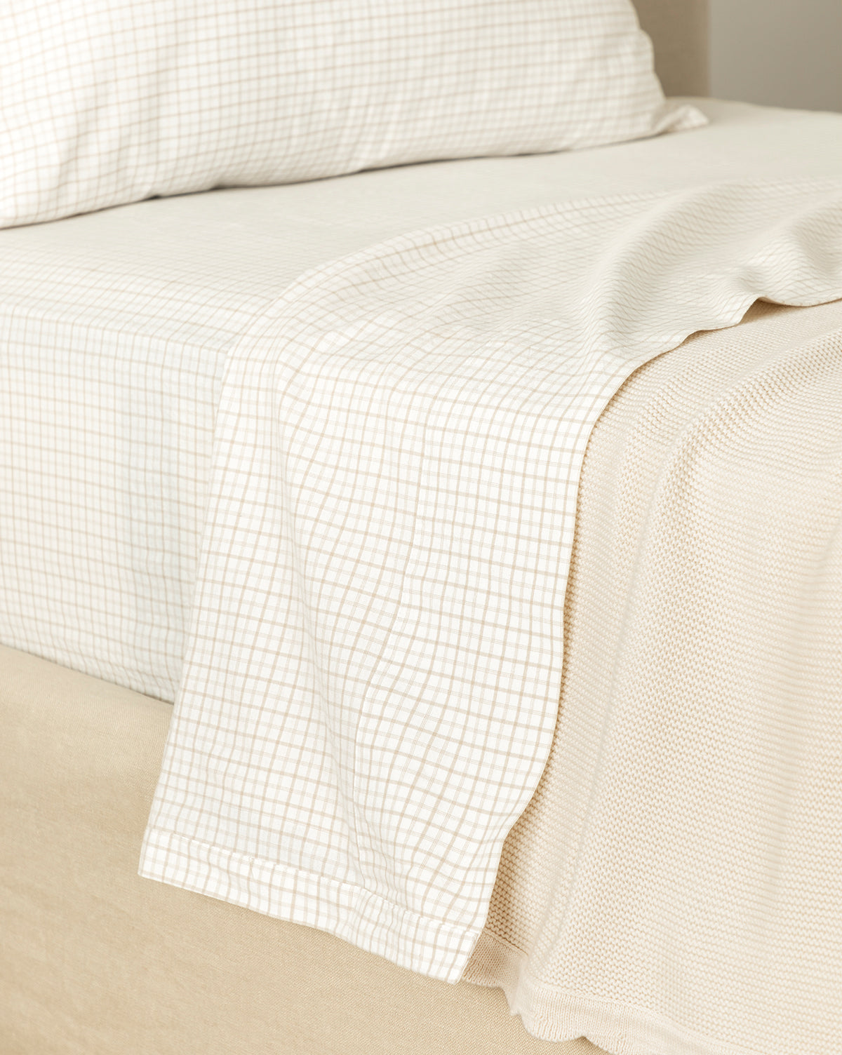 Close-up of a neatly made bed with light grid-patterned cotton sheets and pillow, plus a textured beige blanket at the foot—perfectly showcasing the Nell Twin Kids Sheet Set.