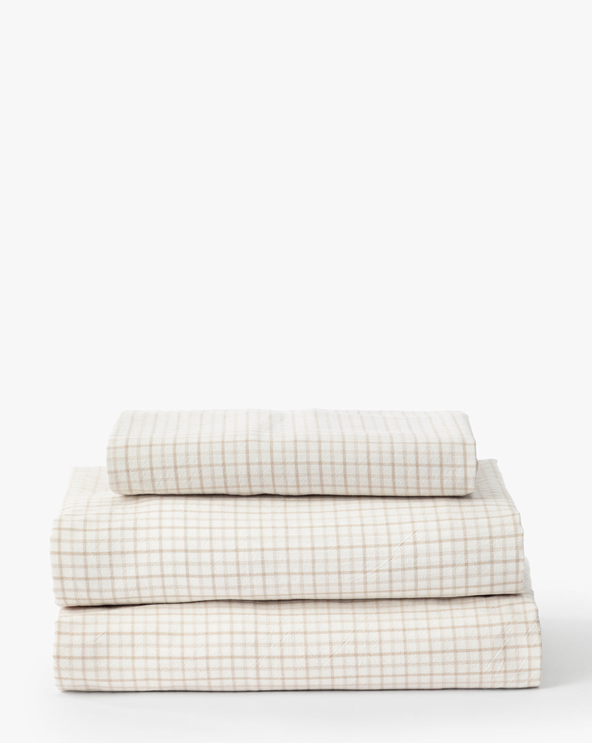 The Nell Twin Kids Sheet Set features cream-colored cotton sheets with a subtle light brown grid pattern, perfectly designed for childrens twin bedding and displayed neatly folded against a plain white background.