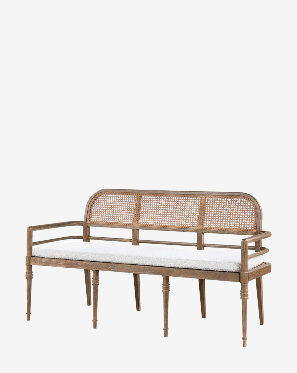 The Nestor Bench features an oak frame, woven cane backrest, straight arms, turned legs, and a white cushioned seat, by McGee & Co.