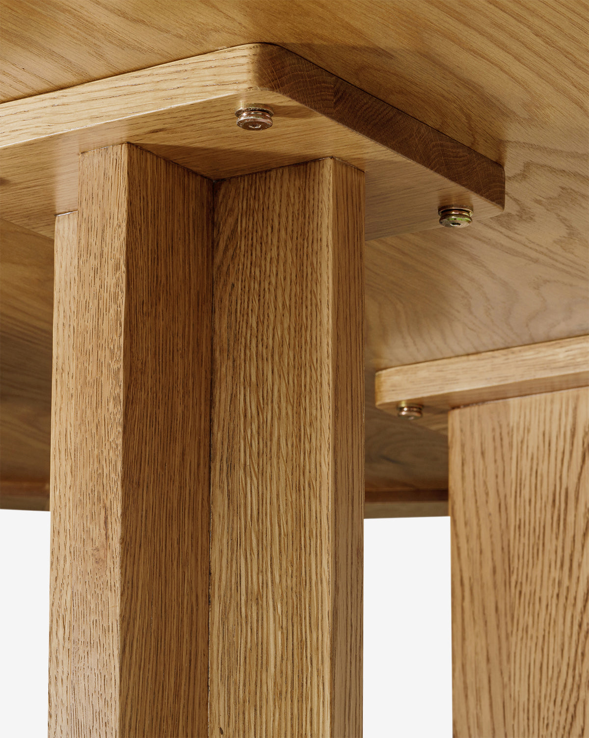 Close-up view of the underside of the Newbold Dining Table, highlighting the honey finish, visible screws, and natural wood grain texture where two legs meet and attach to the tabletop, by McGee & Co.