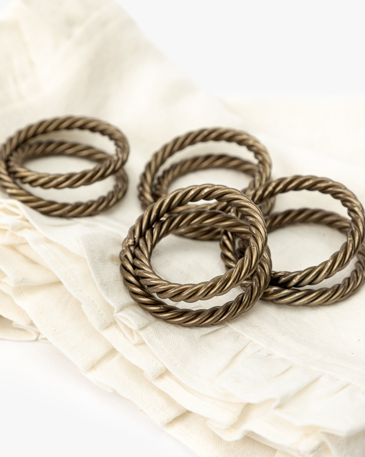A set of four Nichols Napkin Rings sits atop folded cream-colored, ruffle-edged napkins, creating an elegant table setting against a simple white background, by McGee & Co.