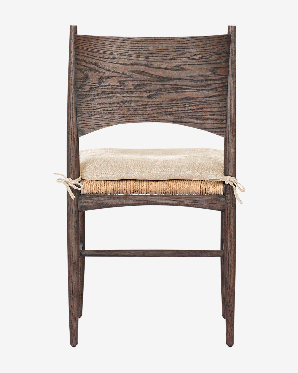 The Nixie Dining Chair is made of solid oak with a curved backrest, straight legs, and a light woven banana leaf seat cushion tied to the back legs, by McGee & Co.