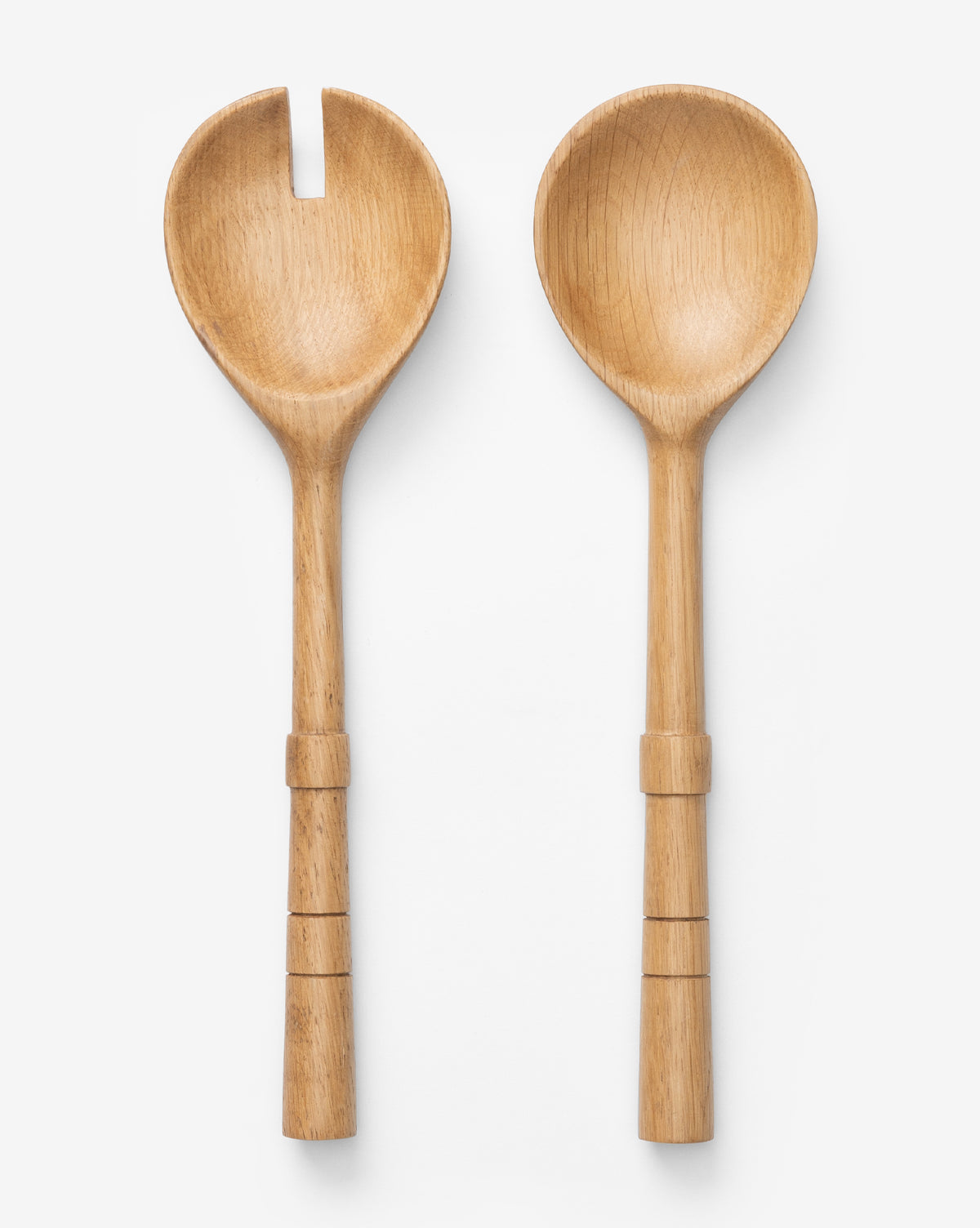 The Notched Oak Wood Salad Servers rest on a white background—one is a fork, the other a spoon. Both have rounded, notched handles with carved rings, creating an elegant and organic serving set by McGee & Co.