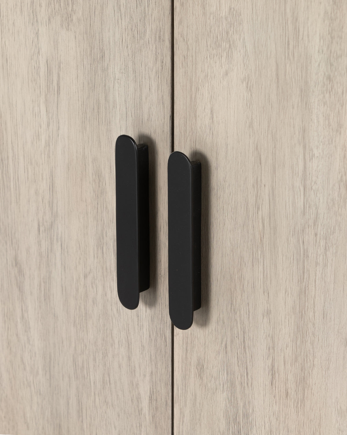 Close-up of two black vertical handles on light wood cabinet doors with subtle grain, part of the Nyx Sideboard featuring adjustable shelves for versatile storage, by McGee & Co.