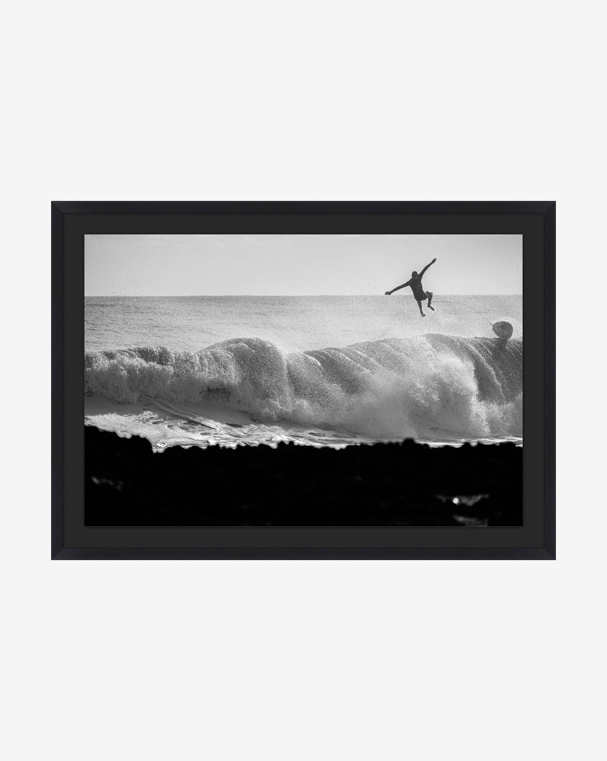 Ocean Nights No. 3 is a striking black and white photo of a surfer leaping off a board above a crashing wave, with dramatic spray and silhouetted rocks—a gallery-quality print from the renowned Ocean Nights series, by McGee & Co.