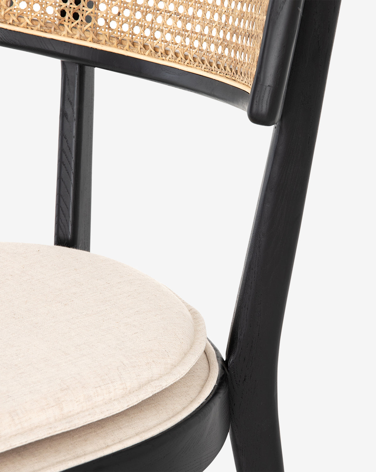 Close-up of the Odelle Dining Chair, featuring a black wooden frame, woven cane backrest, and round beige seat cushion. This modern dining chair blends timeless elegance with contemporary style, by McGee & Co.