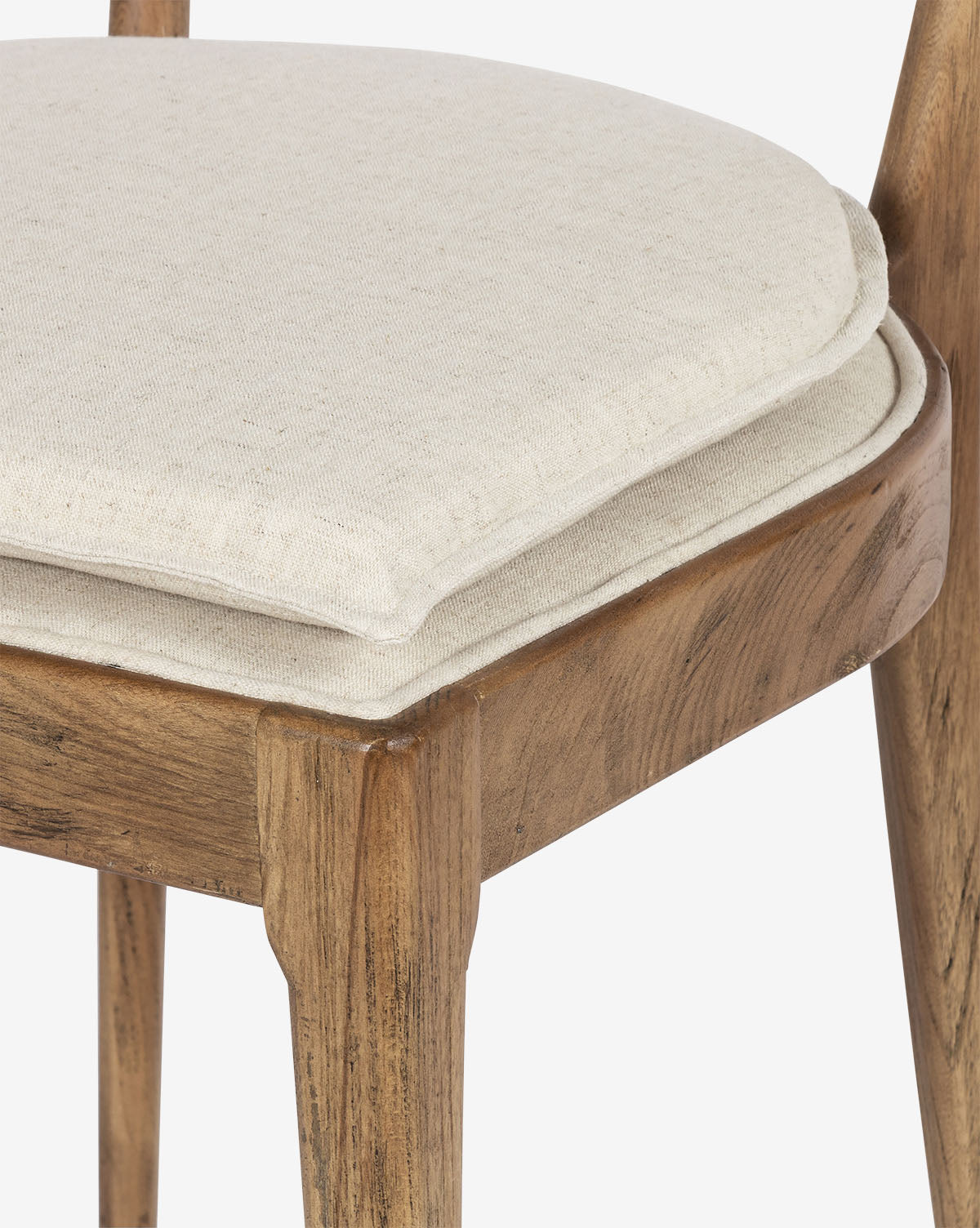 Close-up of the Odelle Dining Chair, showcasing its modern wooden frame, light beige upholstered seat with extra padding, and detailed fabric texture alongside the natural wood grain, by McGee & Co.