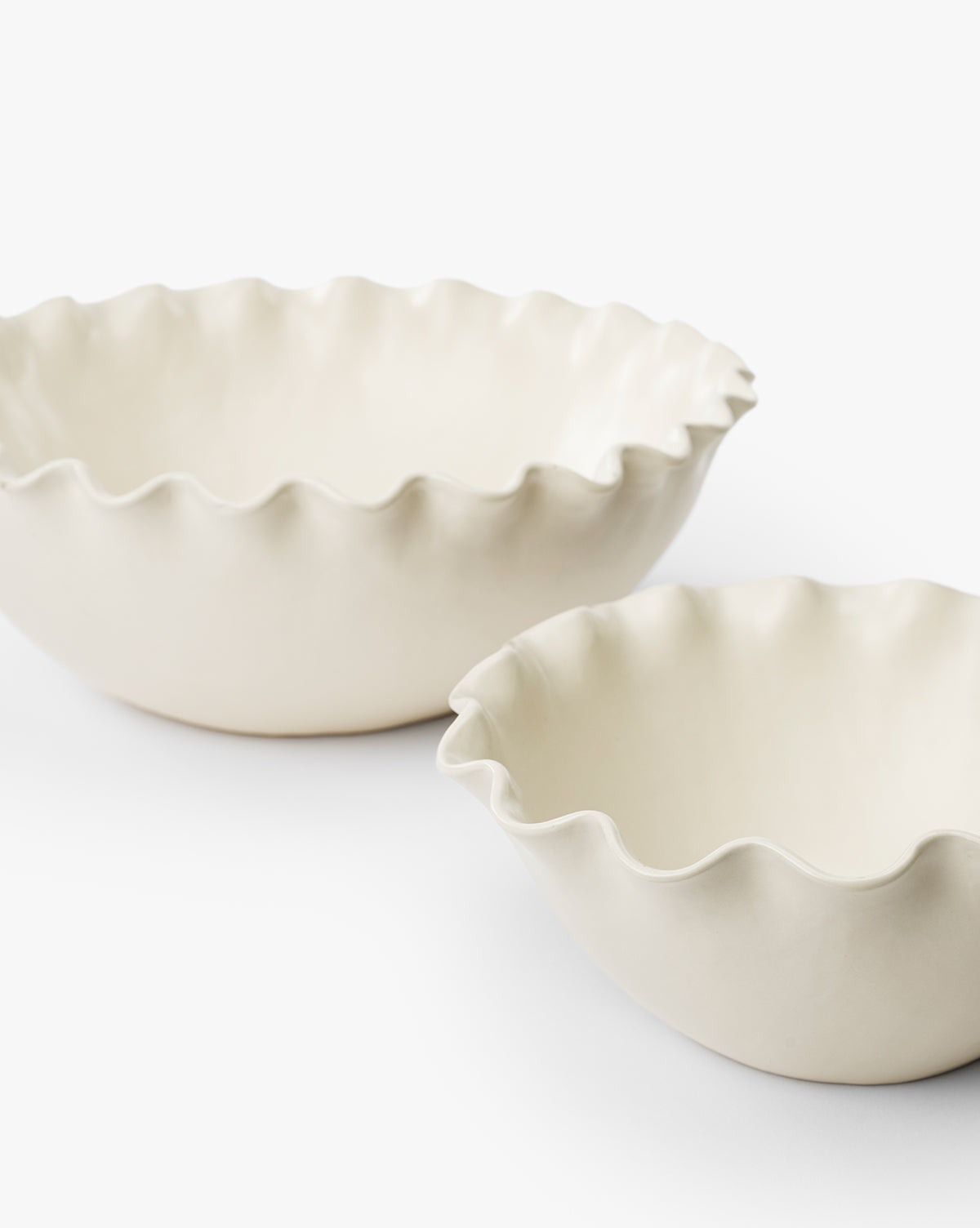 Two off-white Olindo Serving Bowls (Set of 2) with ruffled, wavy edges are placed side by side on a plain white surface, one slightly behind the other. These vintage-inspired bowls are empty by McGee & Co.