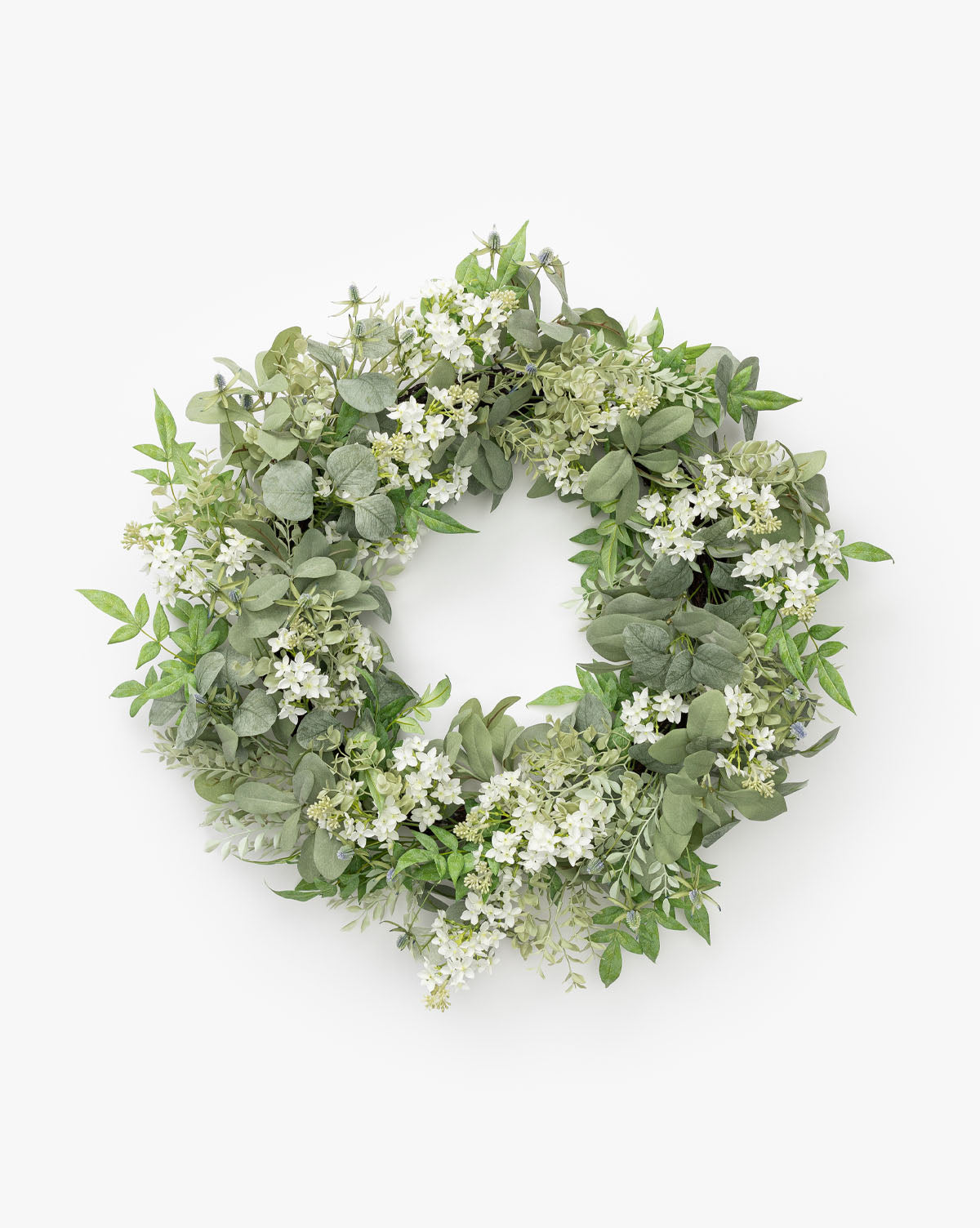 The Orange Jasmine & Eucalyptus Wreath features green eucalyptus leaves and small white orange jasmine flowers, arranged densely in a circular shape against a plain white background.