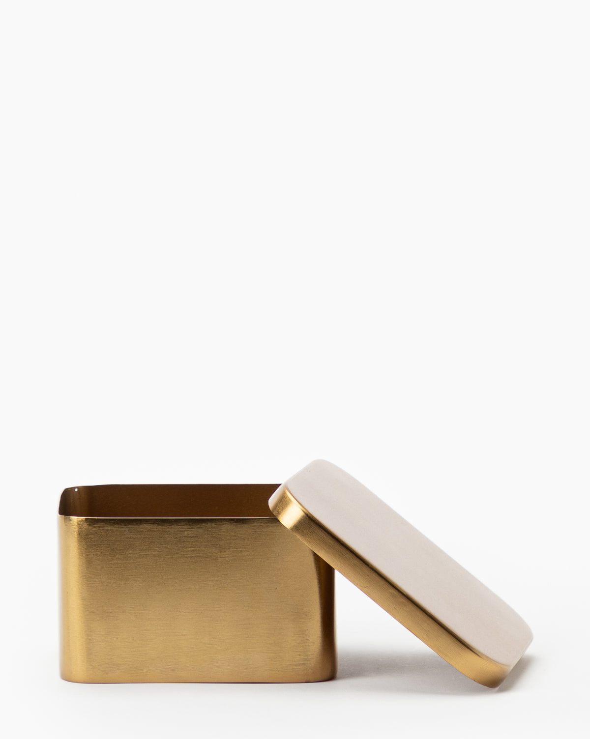 The Oswald Metal Box with a brass finish and rounded edges is shown on a plain white background, its matching white lid leaning against it.